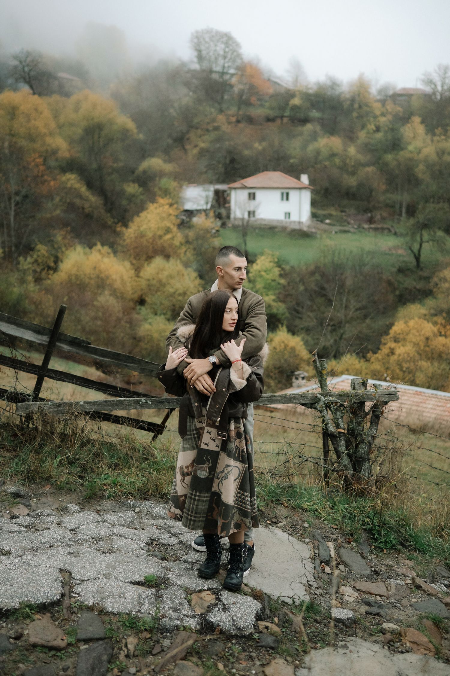 A hunter in camouflage gear walks along a rocky path through an autumn forest landscape.