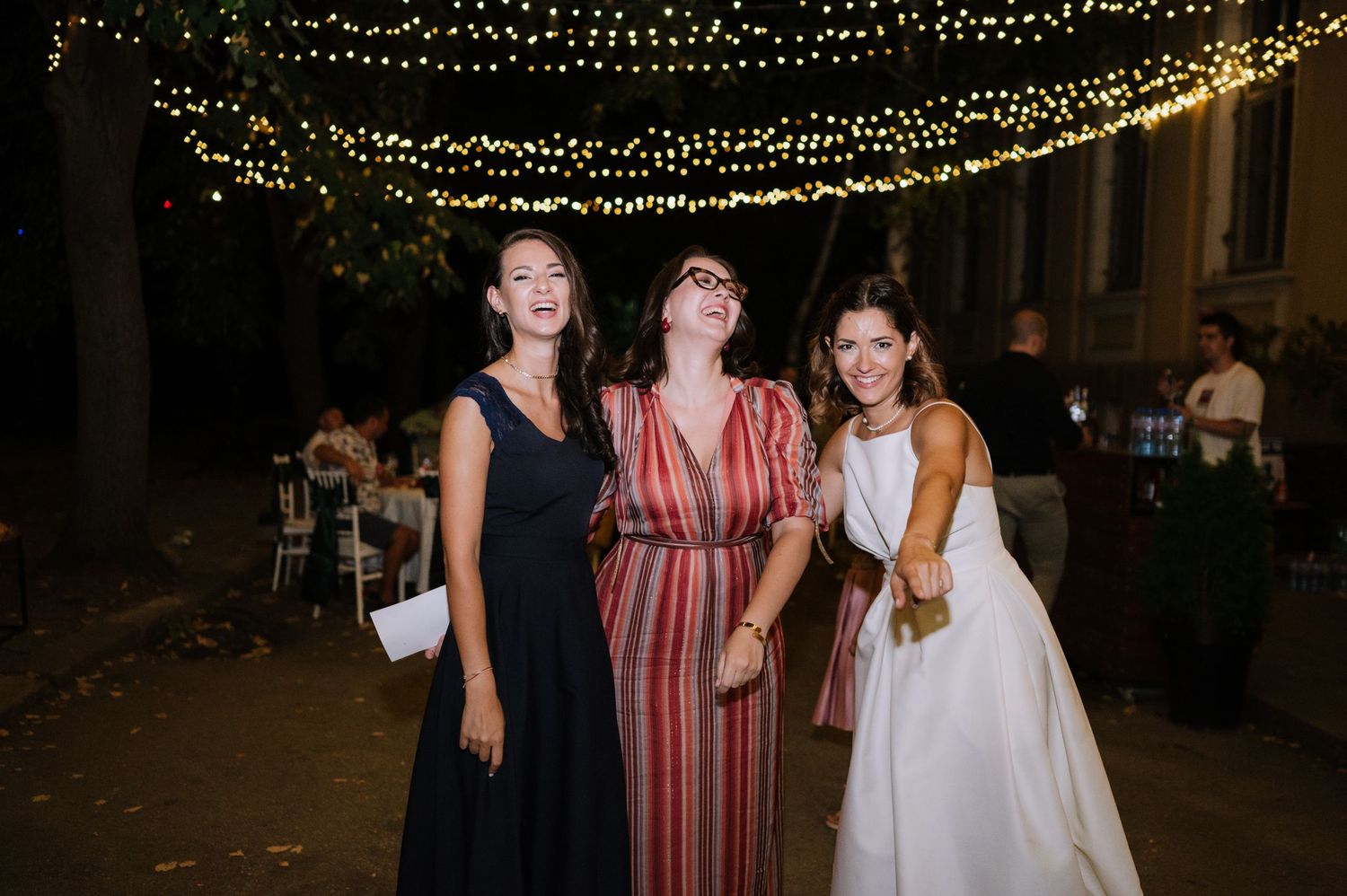 People enjoying a festive outdoor event at night under decorative string lights.