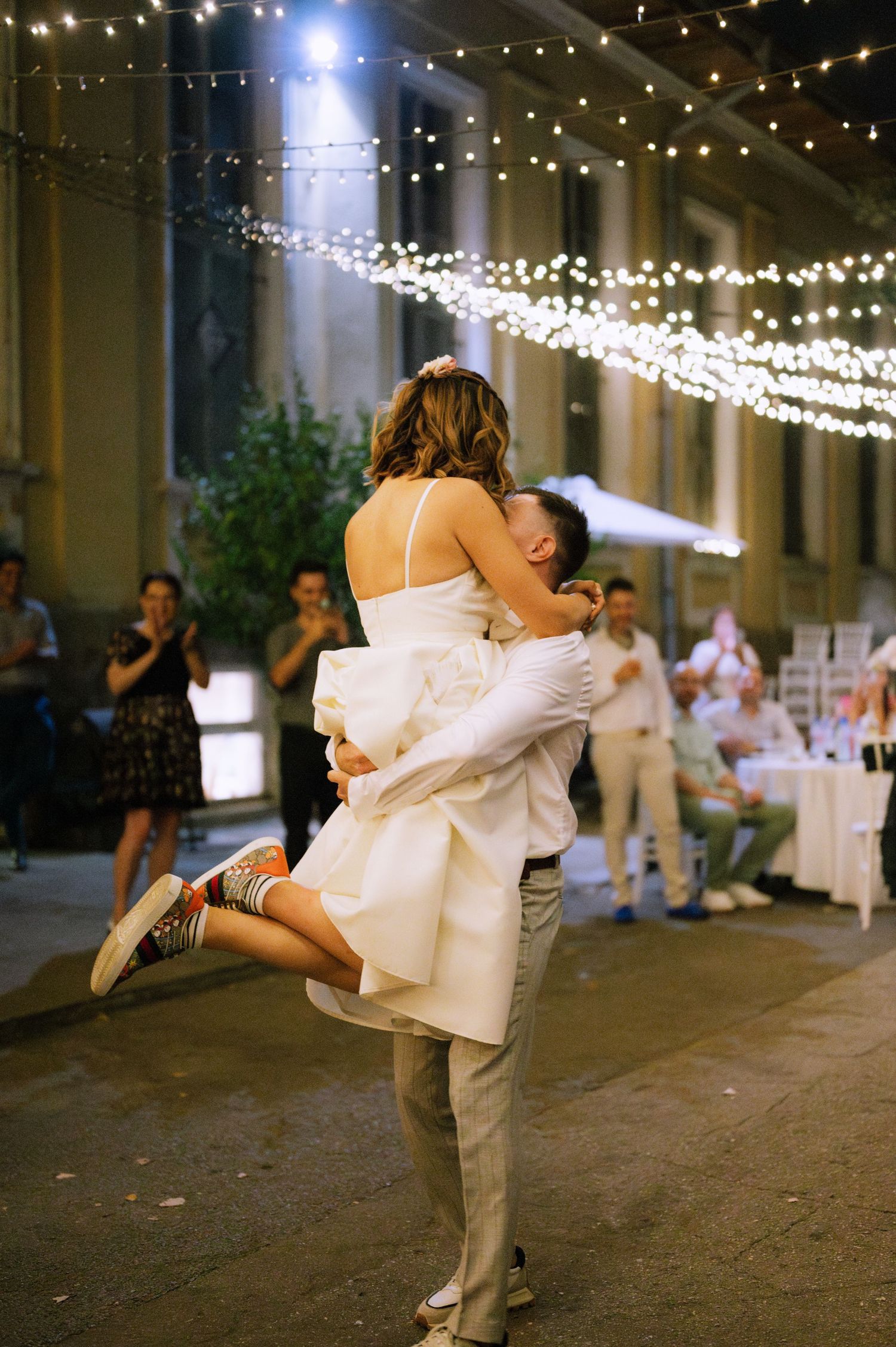 A couple shares a romantic dance move at a wedding reception under twinkling string lights.