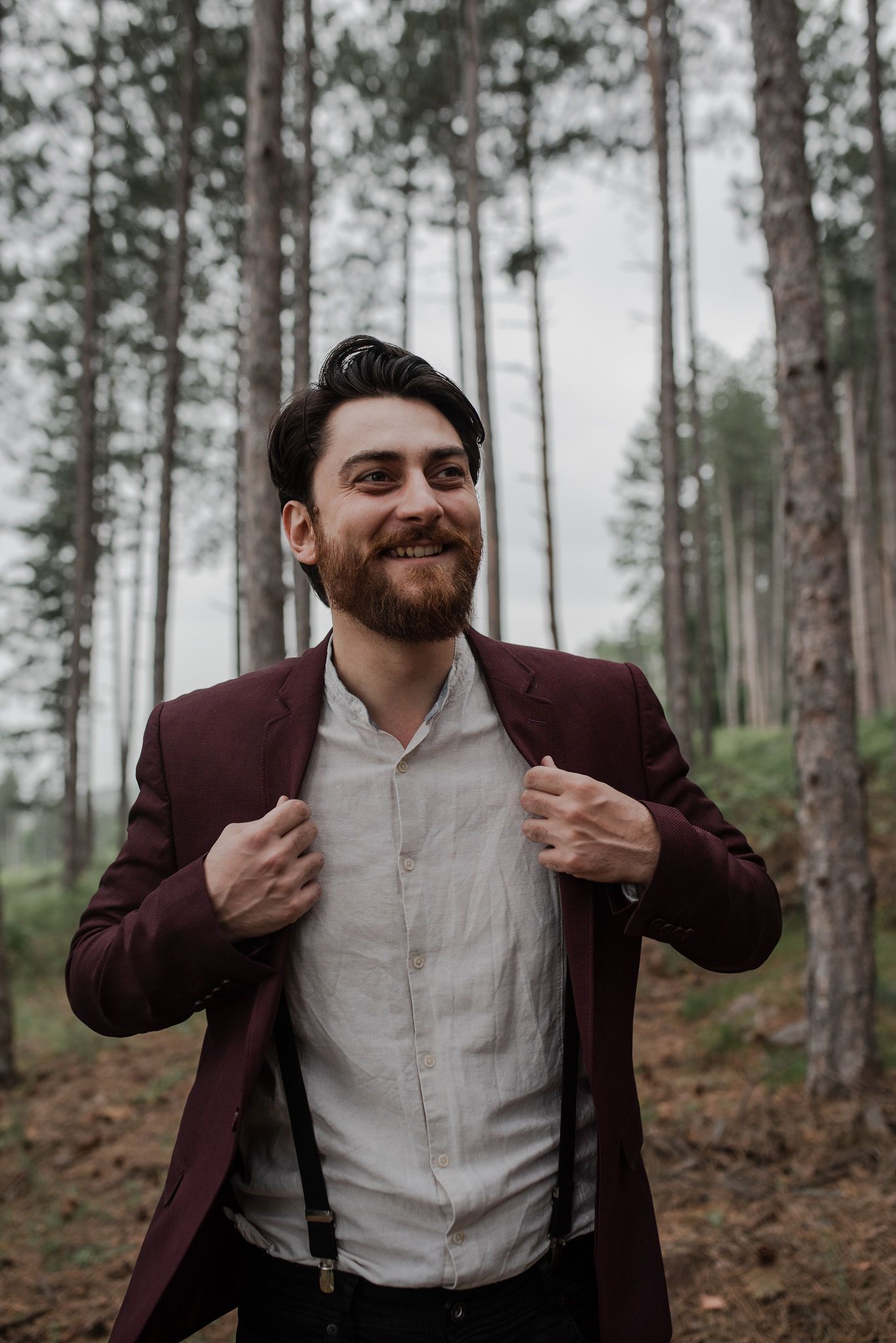 A smiling person in a burgundy blazer and white shirt poses in a misty forest setting.