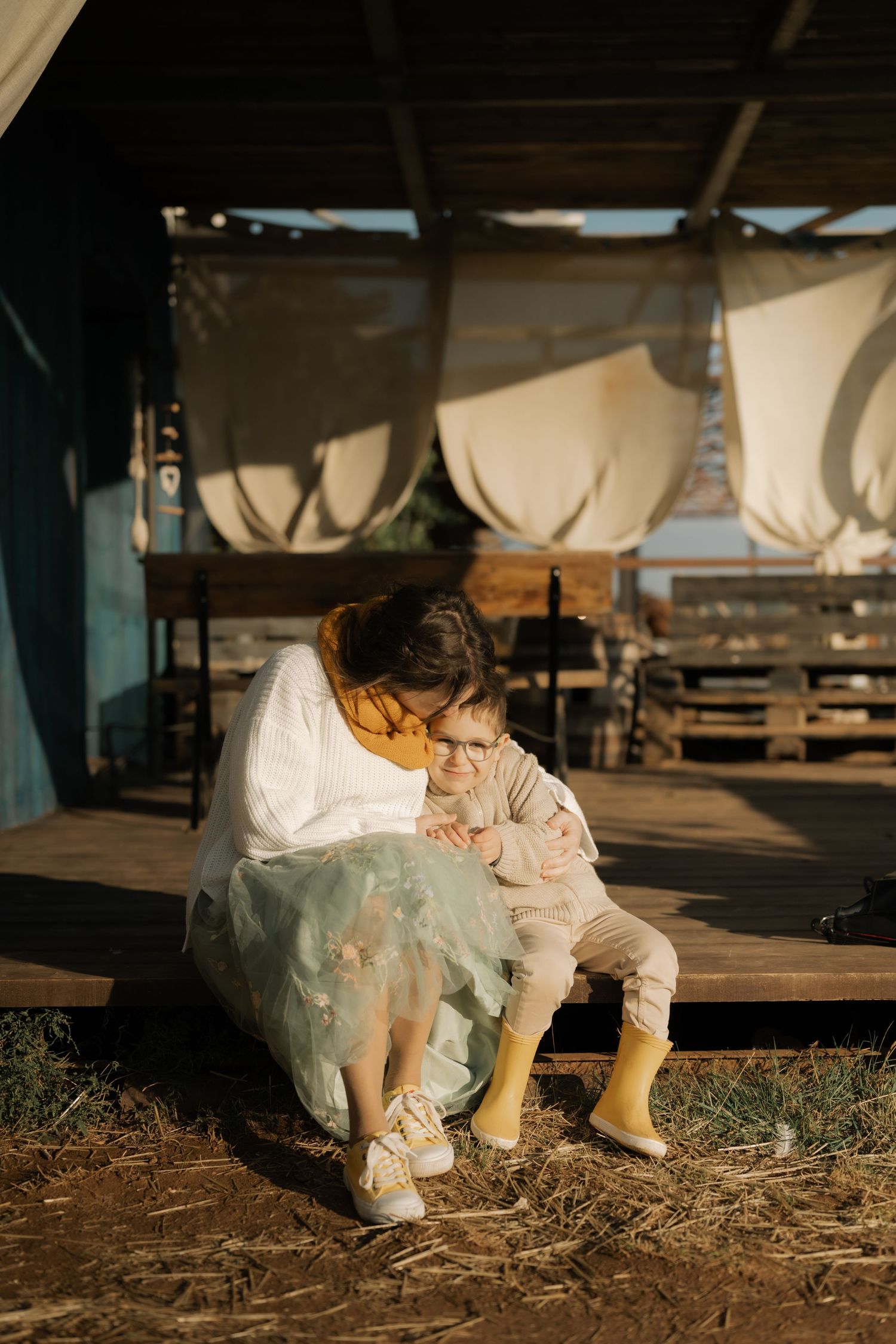 A child in white clothing sits and plays in the dirt during golden hour lighting.