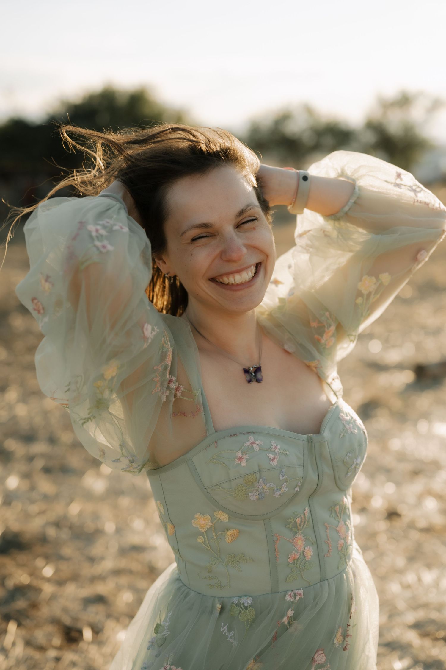 A person in a mint green floral dress twirls joyfully in golden sunlight during a summer photoshoot.