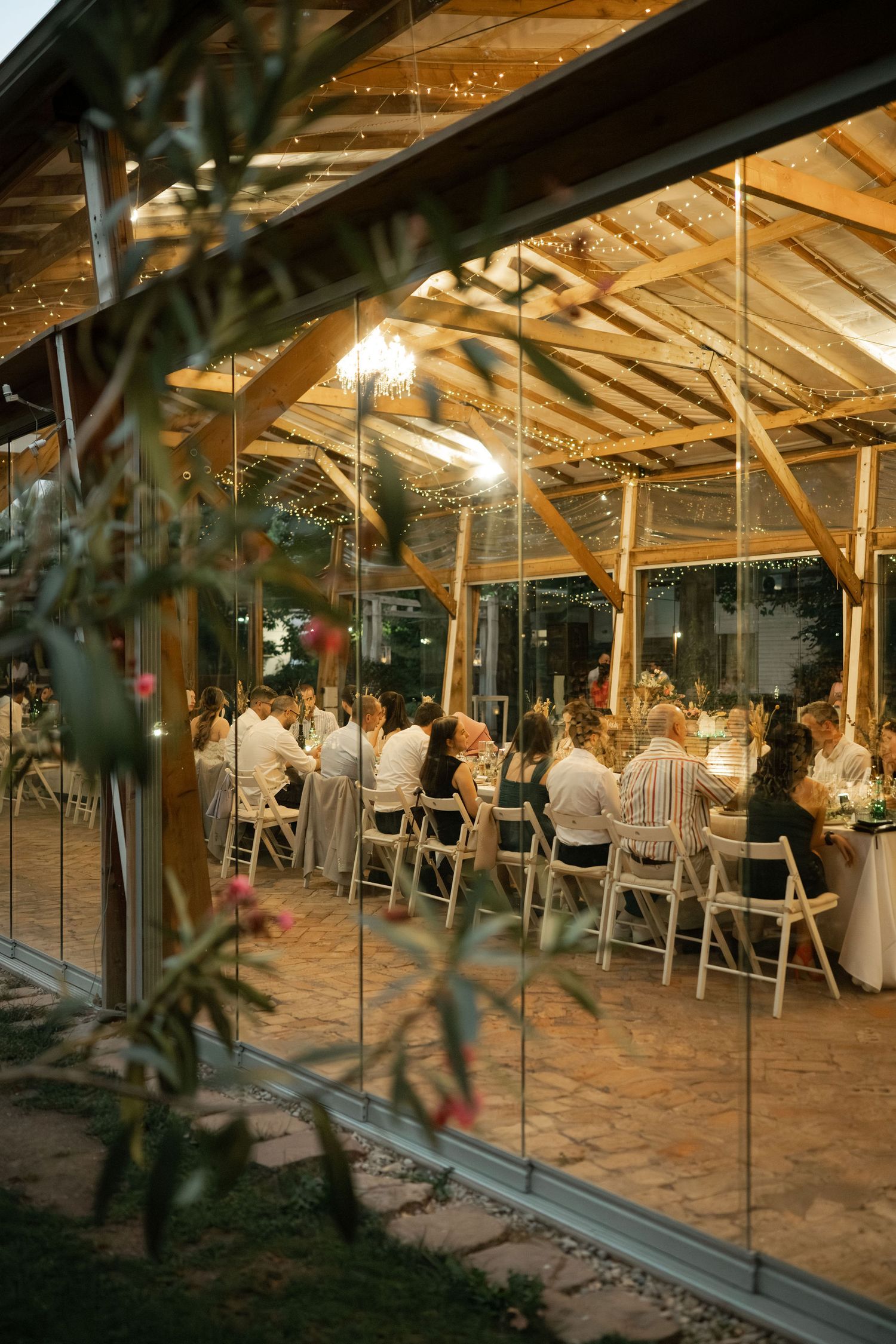 Elegant indoor-outdoor wedding reception venue with glass walls and sandy floors illuminated by warm overhead lighting.