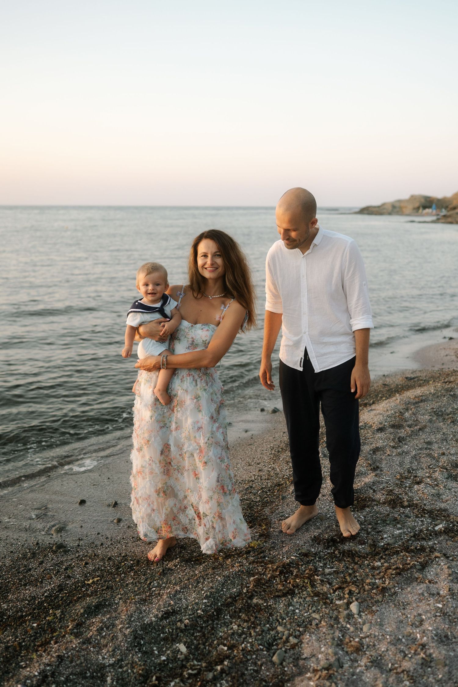 Family walking together on rocky beach at sunset with ocean waves in background.