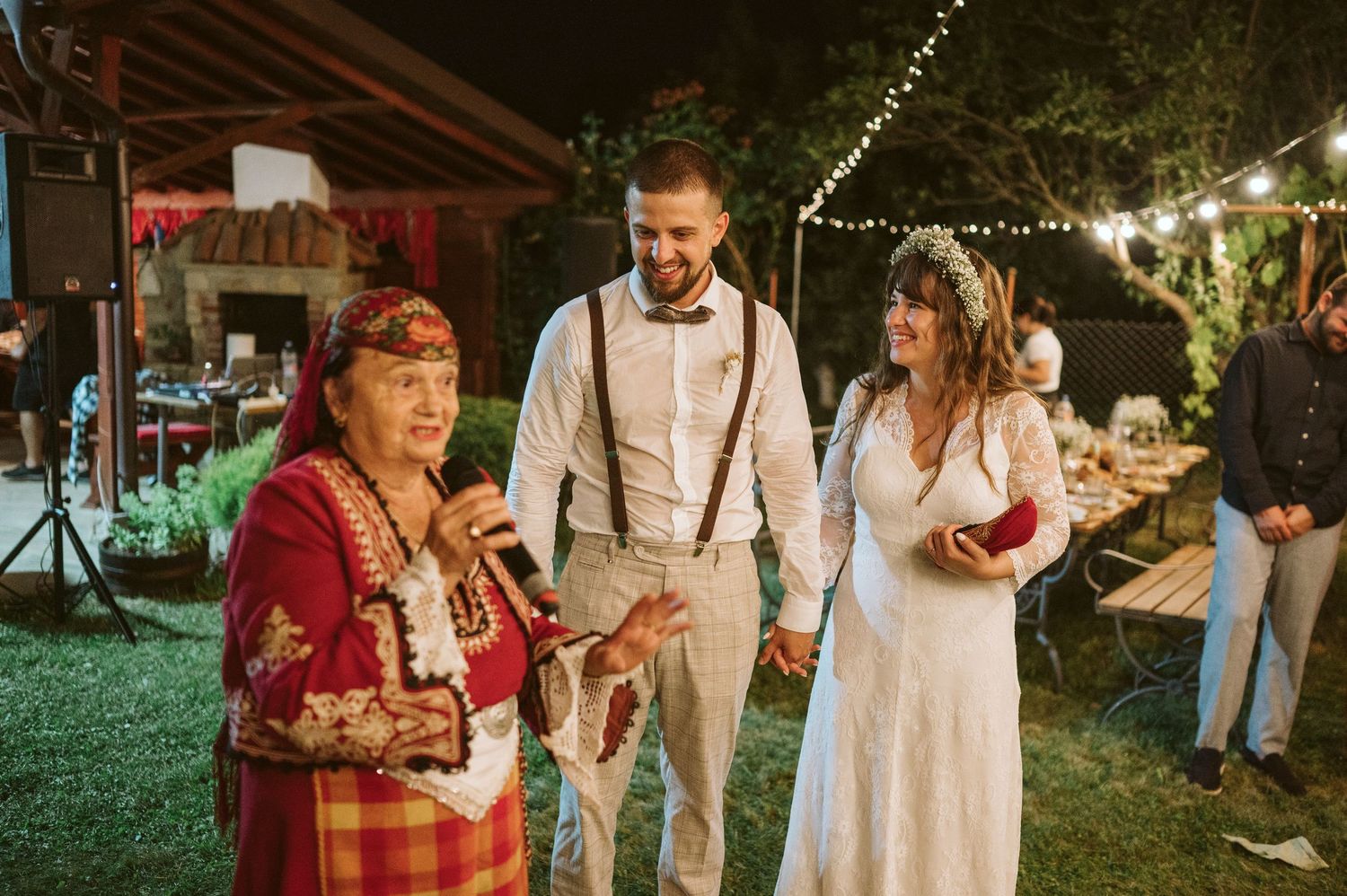 Outdoor wedding reception with string lights and folk entertainment at night.