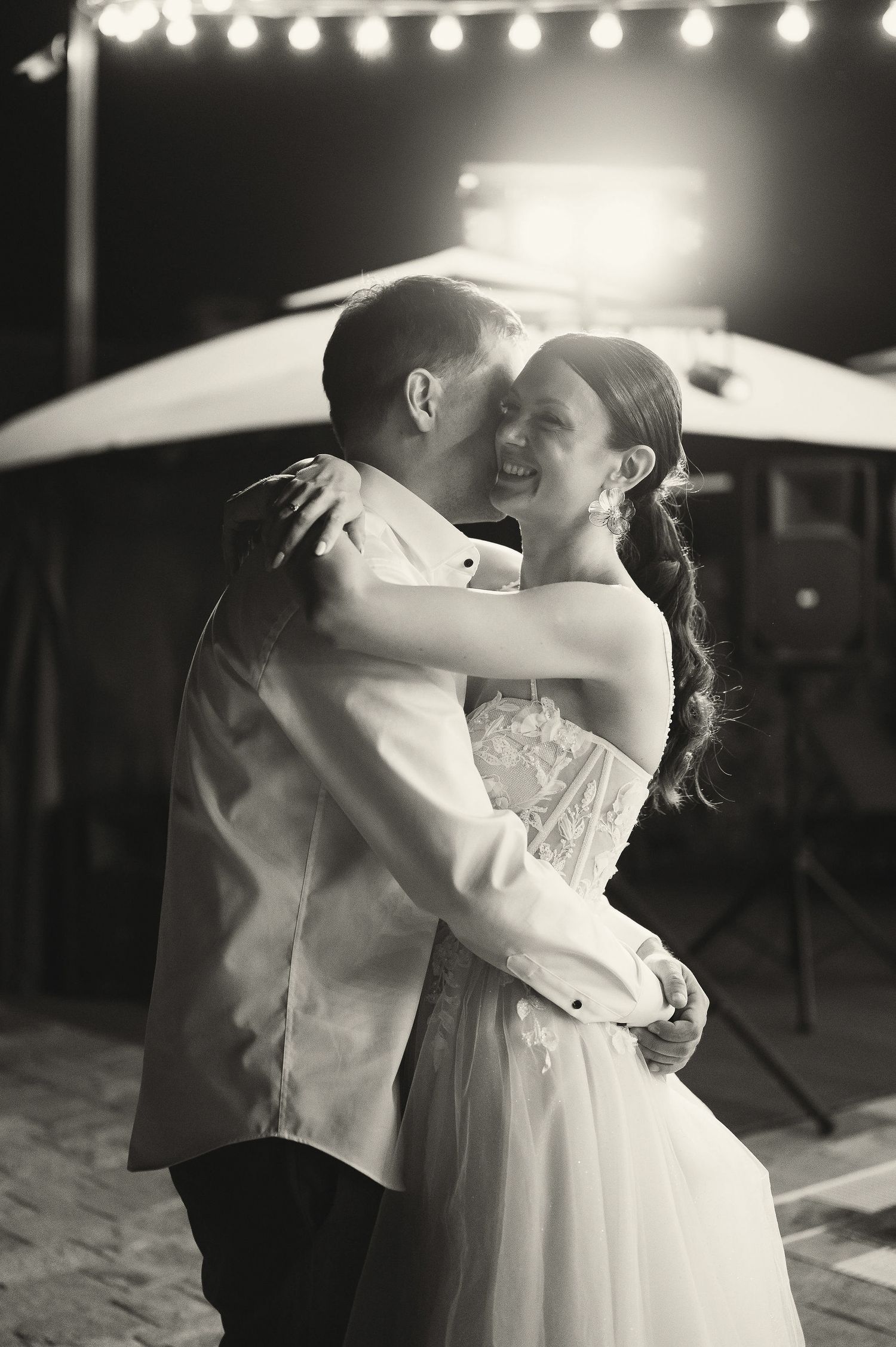 A romantic couple shares a tender dance moment under glowing string lights at an outdoor wedding reception.