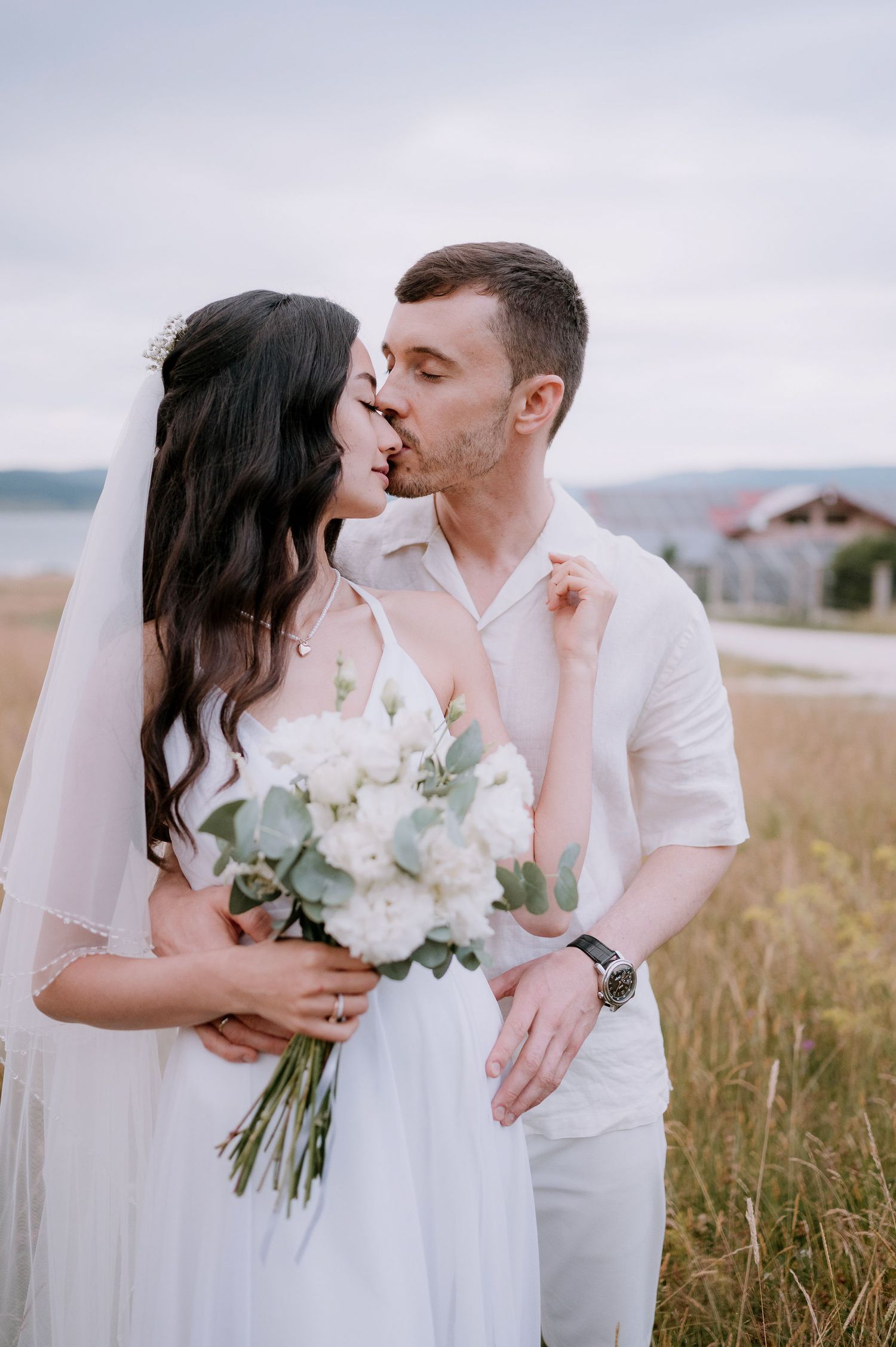 Wedding couple shares romantic moments while holding a bouquet in a scenic meadow.