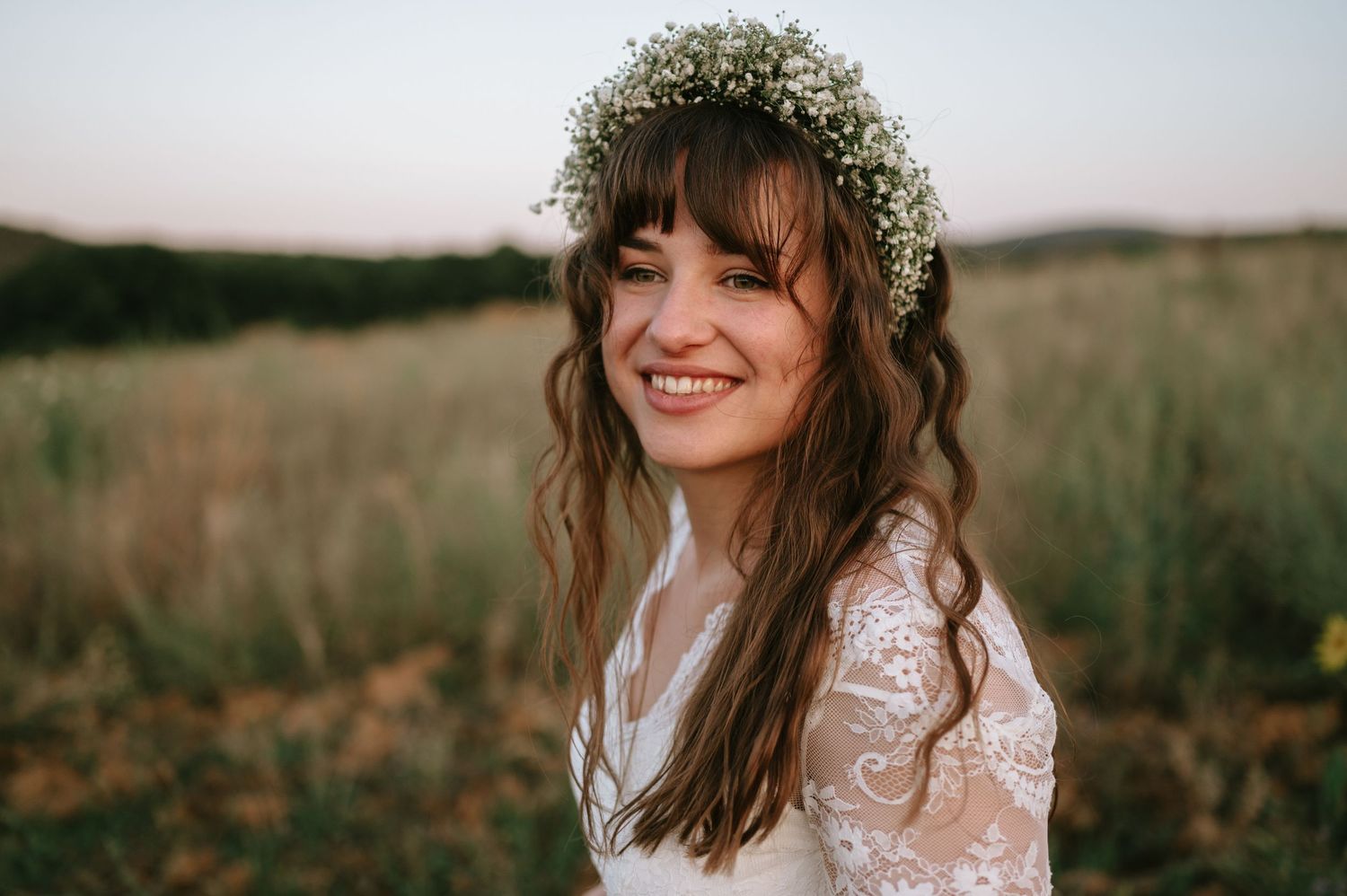 Bride wearing bohemian lace dress and flower crown smiles in golden outdoor light.