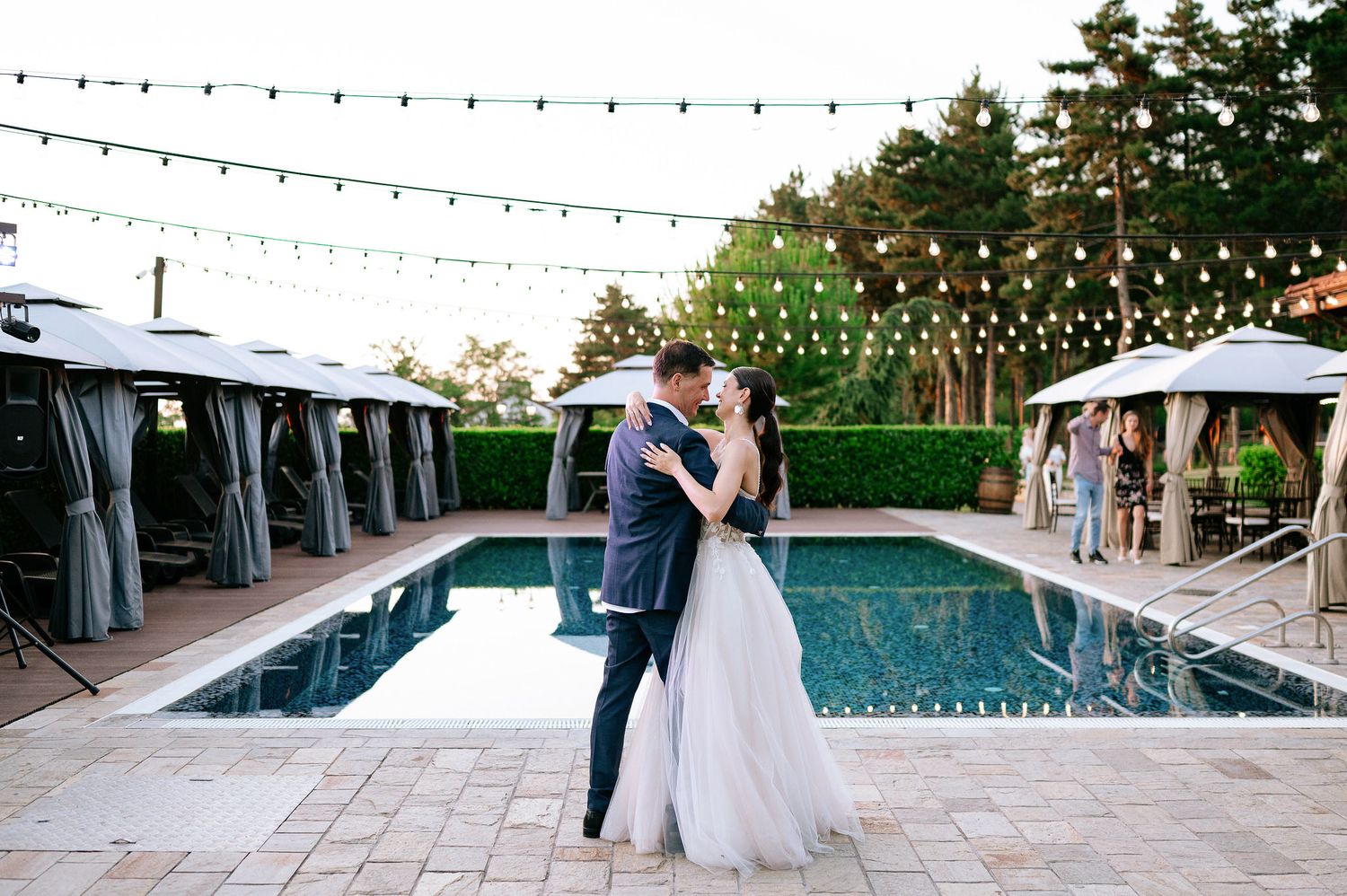 Wedding venue setup with string lights over pool area and stone patio at dusk.