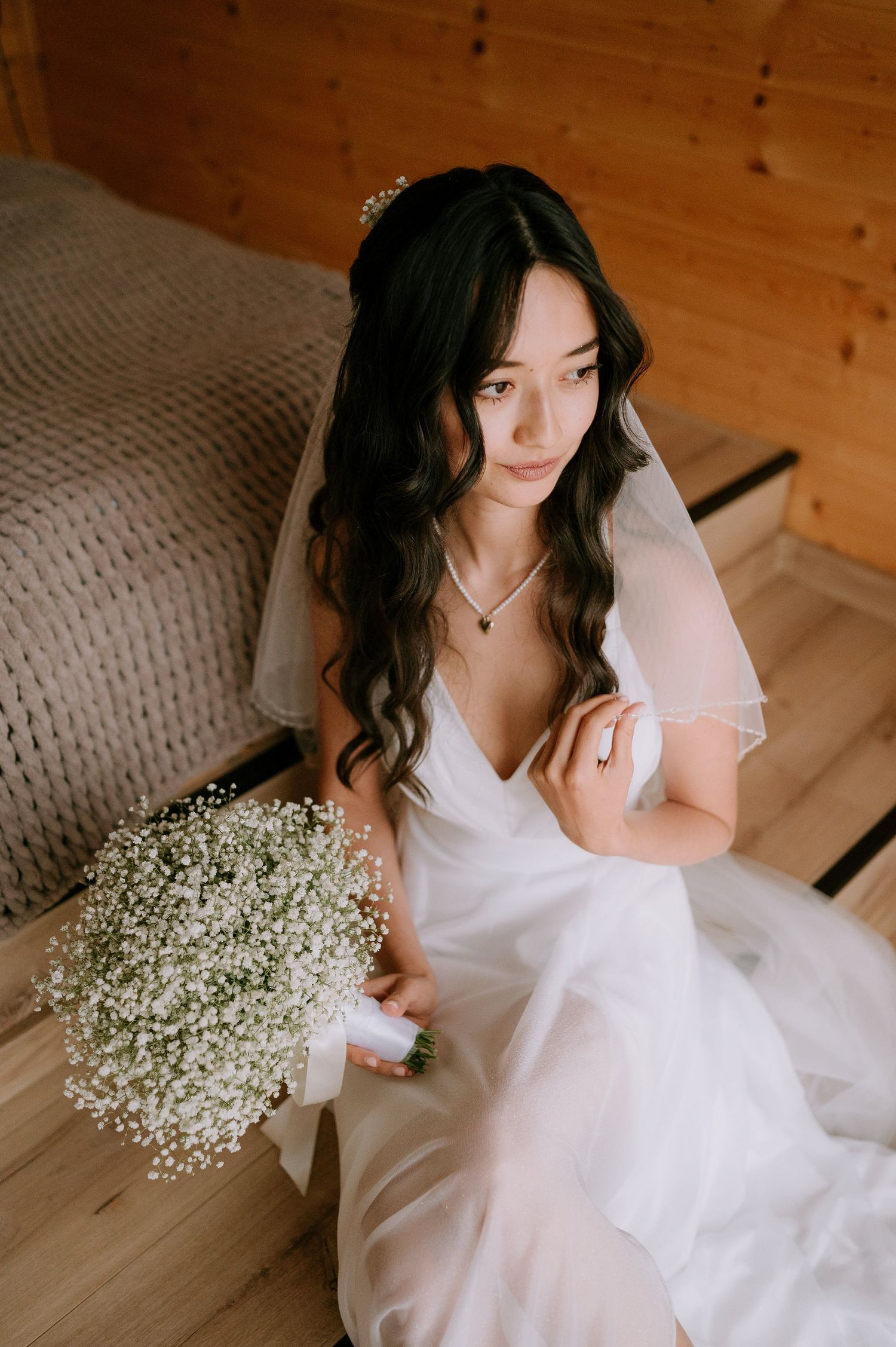 Intimate bridal portrait with flowing white dress and baby's breath bouquet in wooden room.