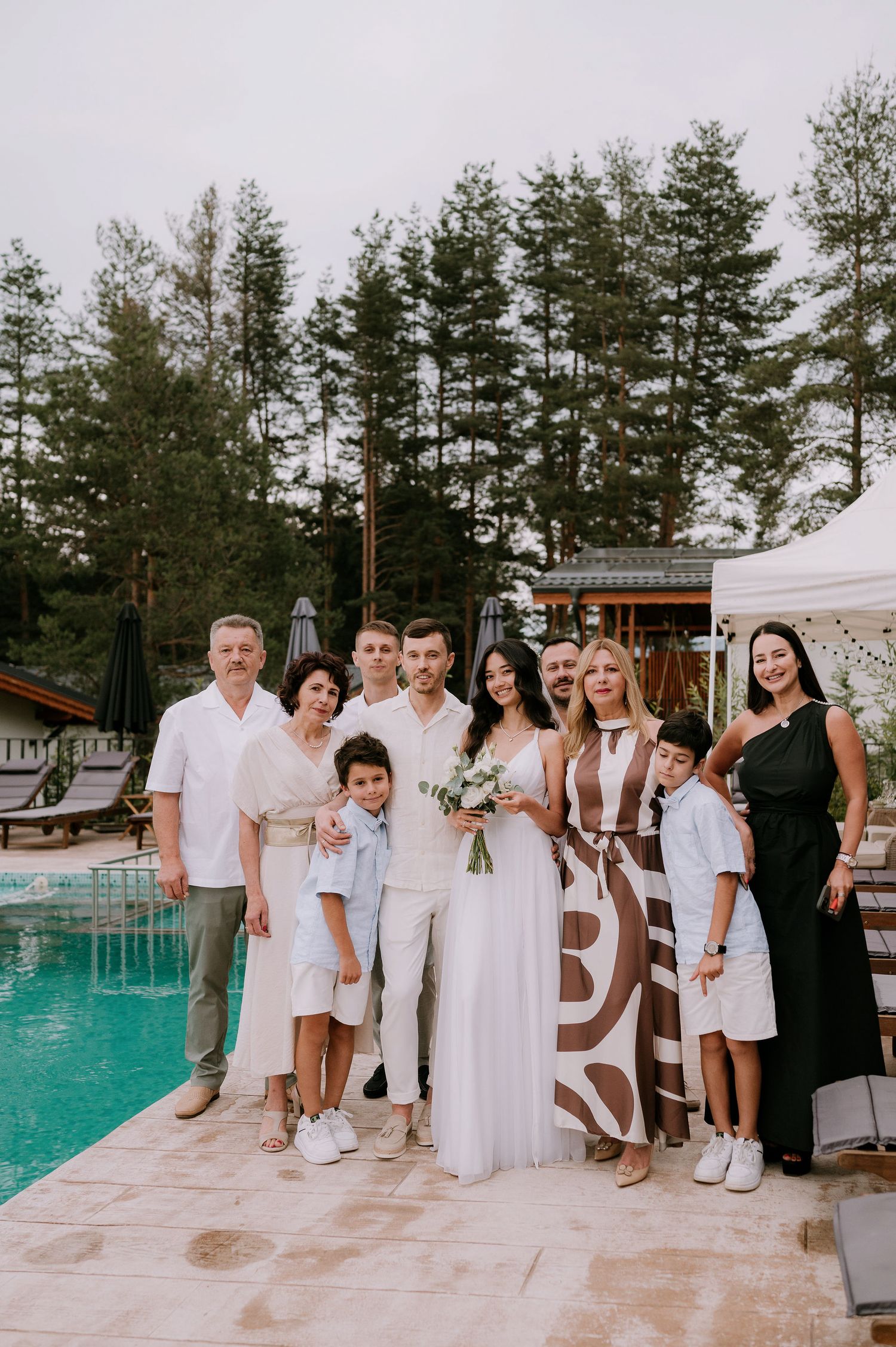 Large group photo of wedding guests dressed in white beside a swimming pool.