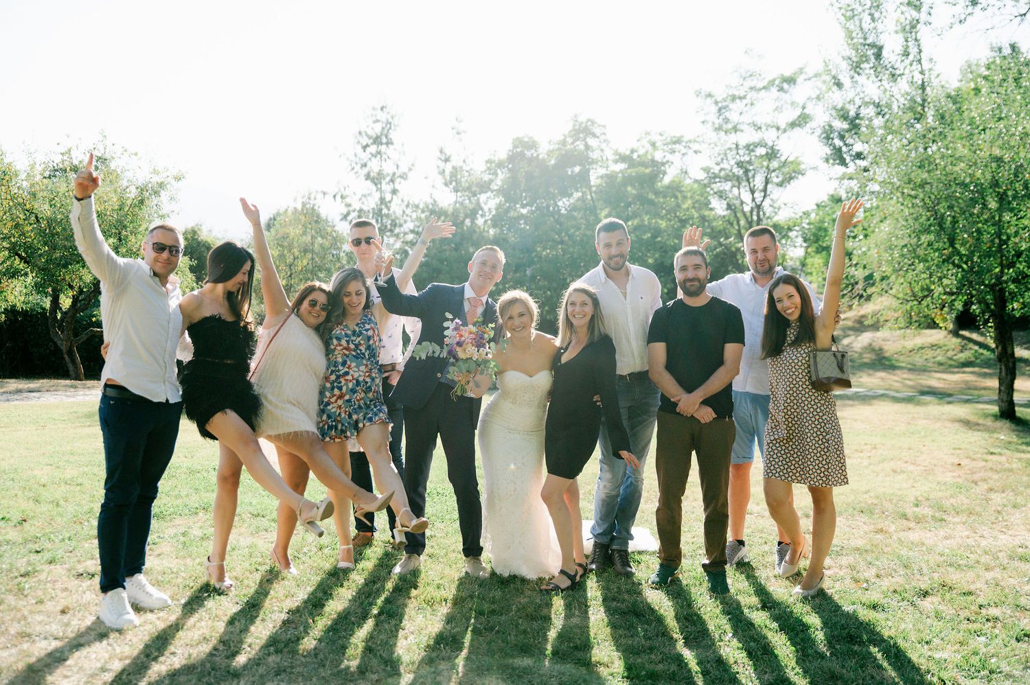 Wedding party members stand together on a grassy hill creating long shadows in evening light.