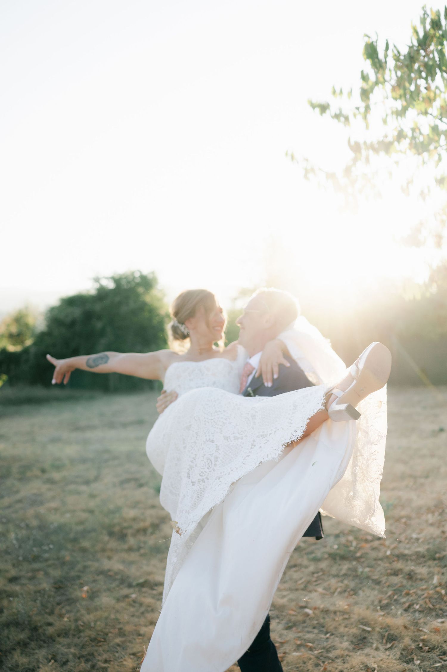 Wedding couple dances playfully in golden sunlight with bride's dress flowing in the breeze.