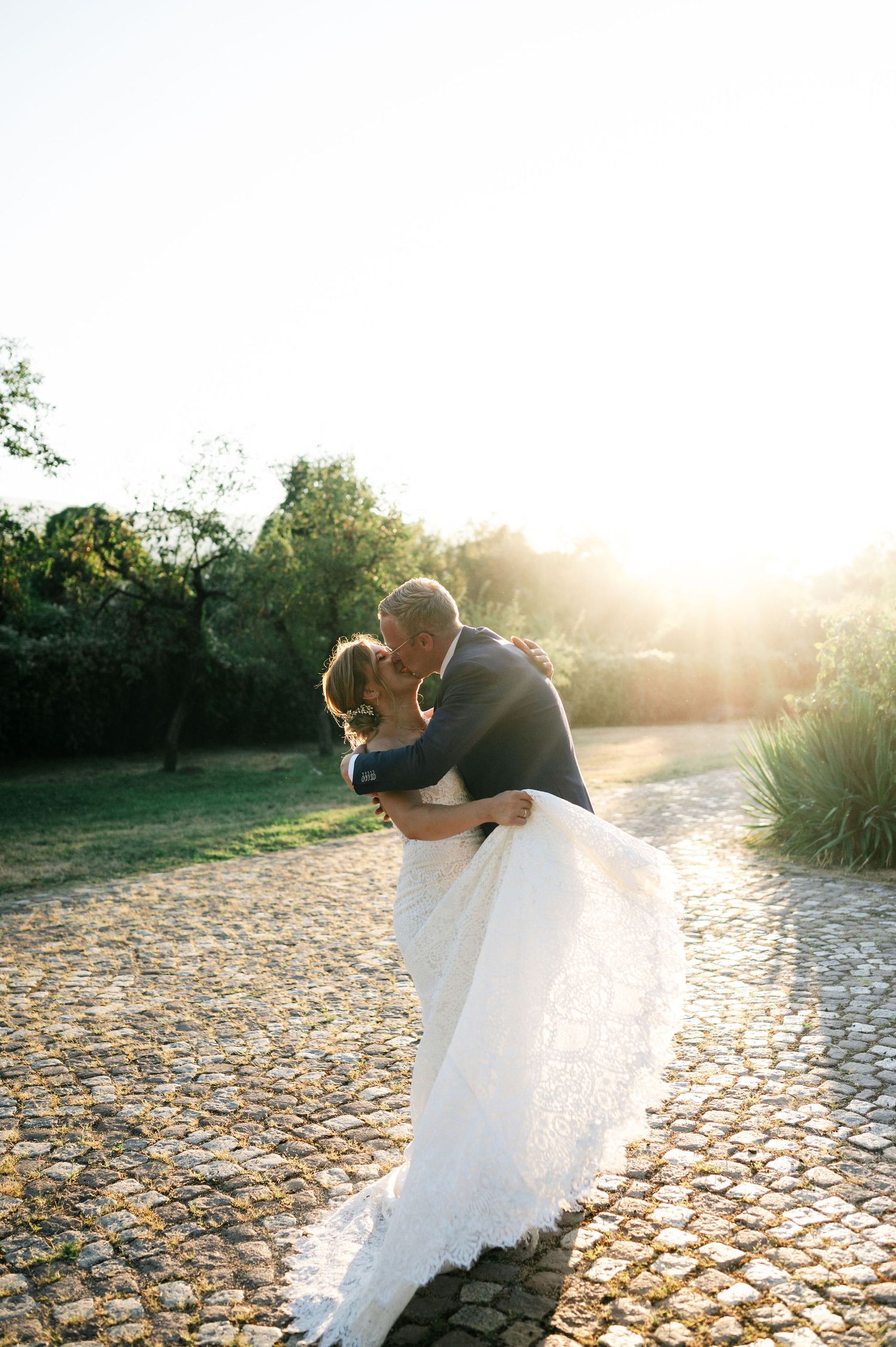 Romantic wedding dance dip captured against golden sunset on cobblestone path.