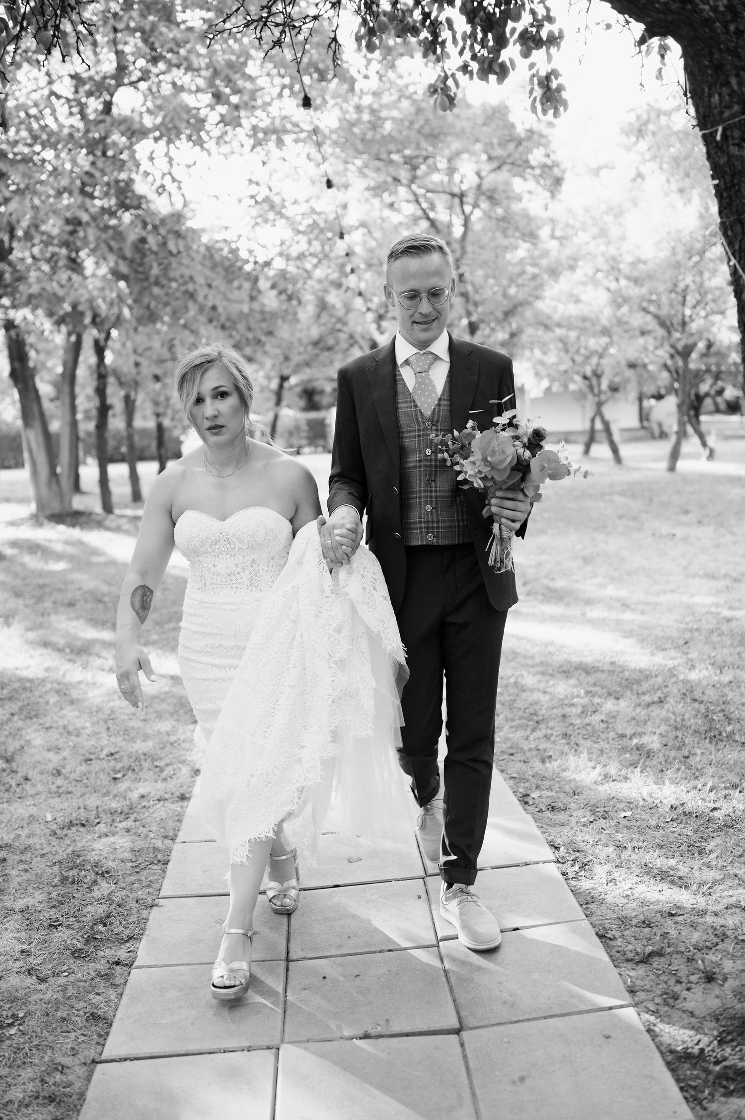 Black and white photo of couple walking on stone path under tree canopy.