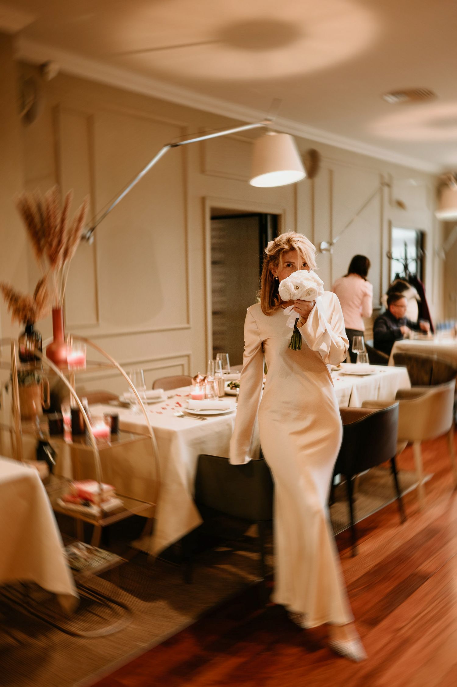 Figures in white dresses move through an elegant room with hardwood floors and paneled walls.