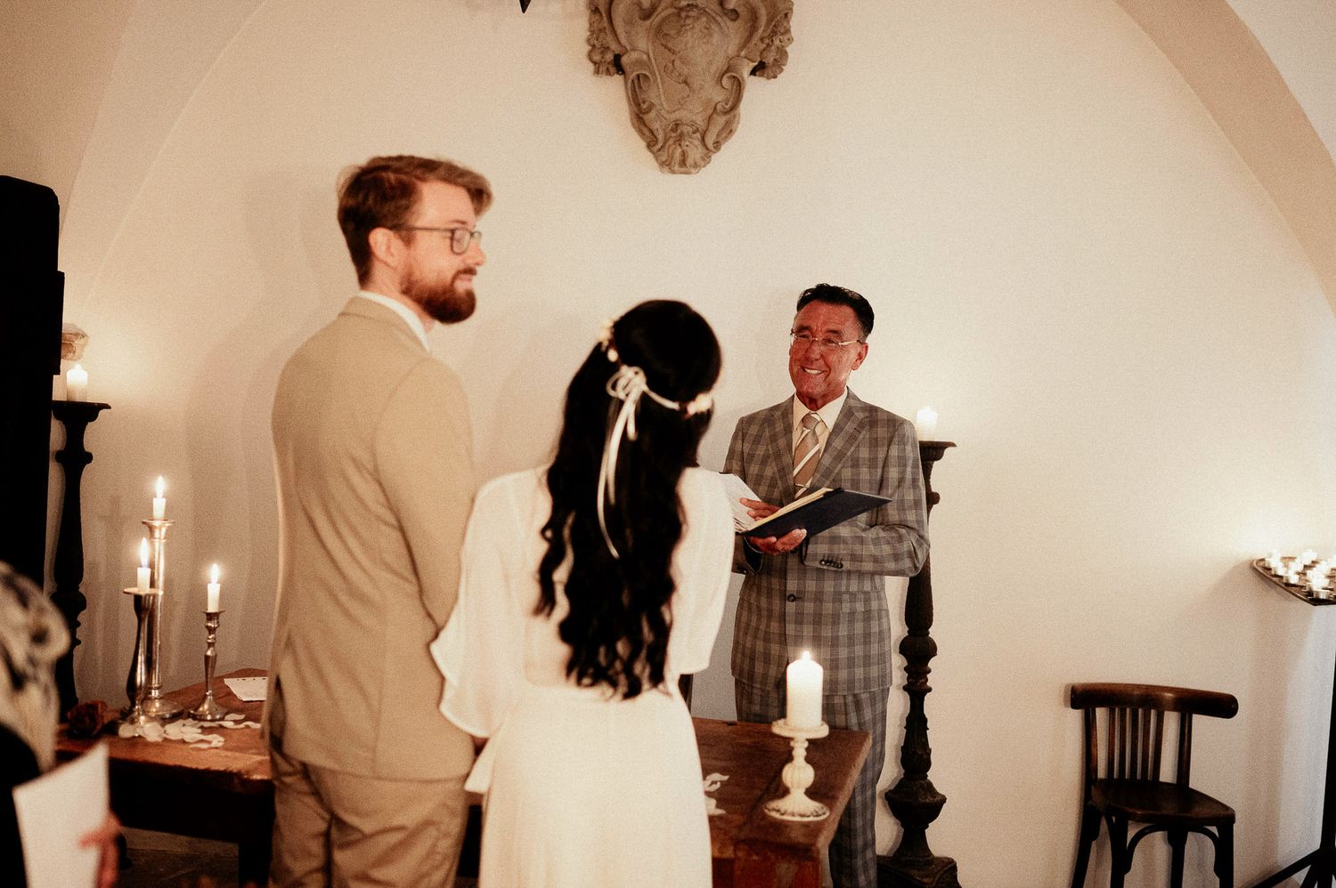 Wedding ceremony in white arched room with candlelight and vintage furniture.