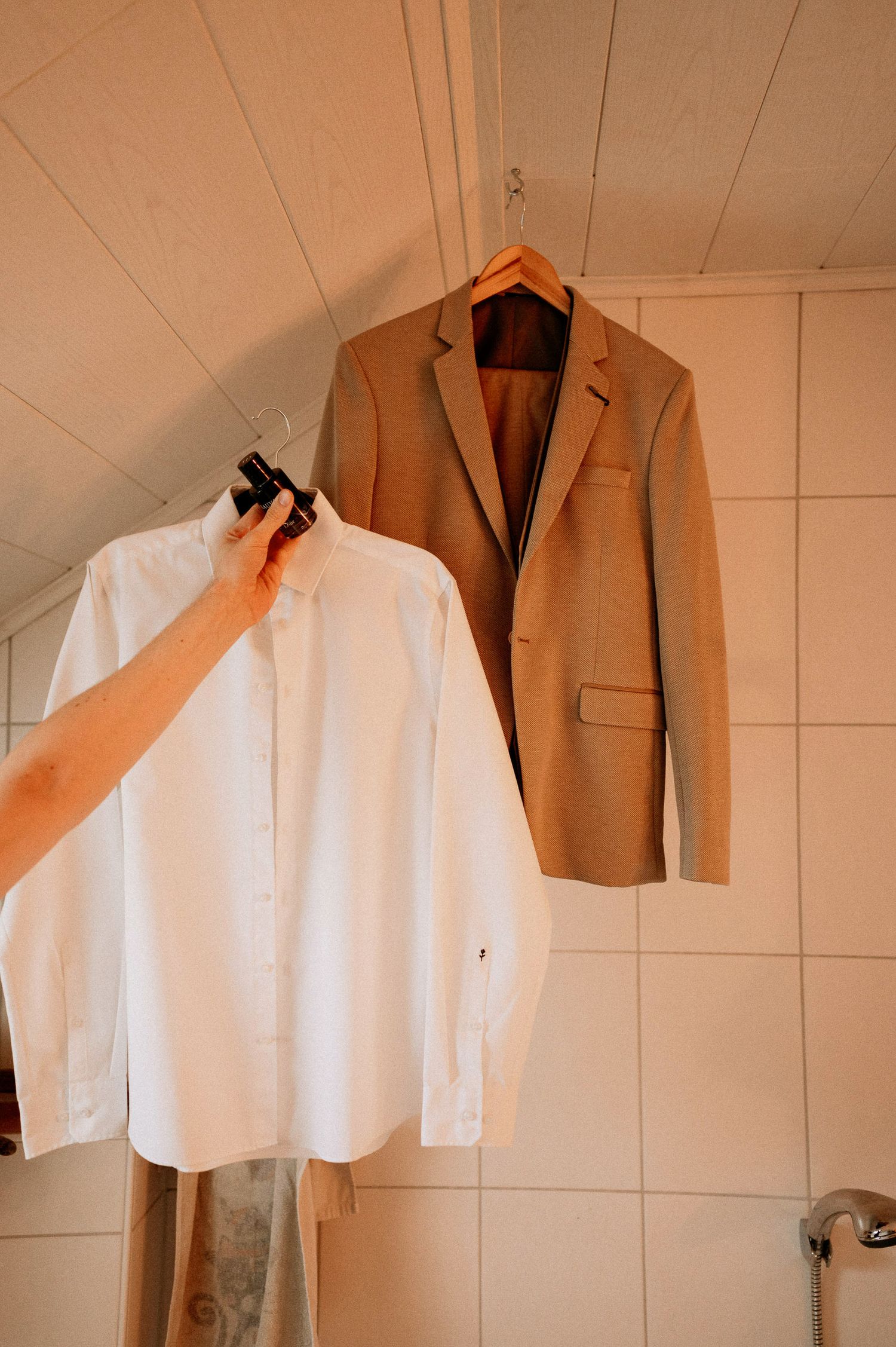 A white dress shirt and tan suit jacket hanging on display against a wall.