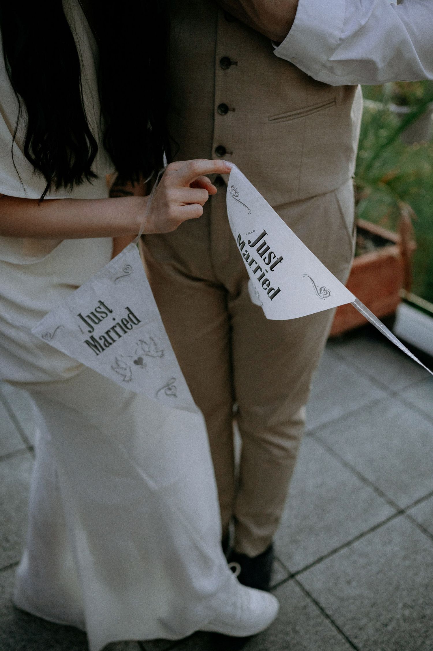 Close-up of wedding couple holding 'Just Married' paper banners on outdoor terrace.