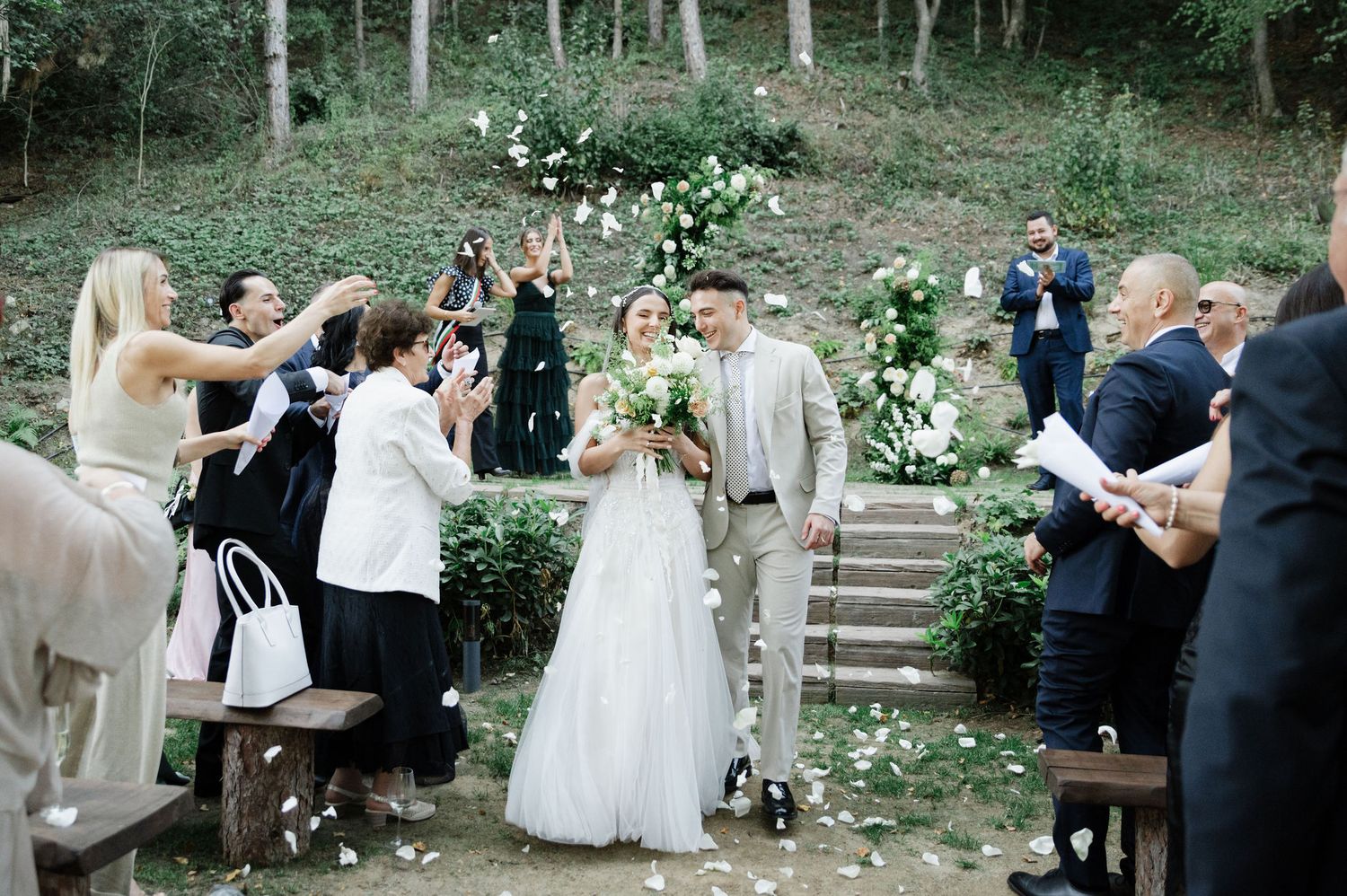 Guests celebrate at an intimate forest wedding venue with stone steps and decorative floral arrangements.