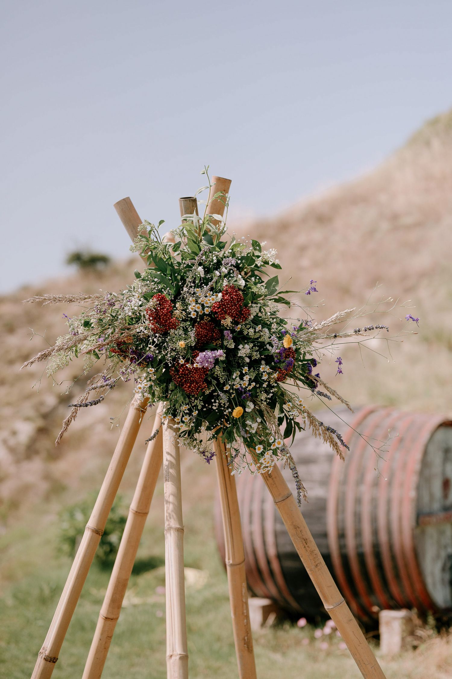 Rustic wooden arch decorated with wildflowers and greenery against a natural backdrop.