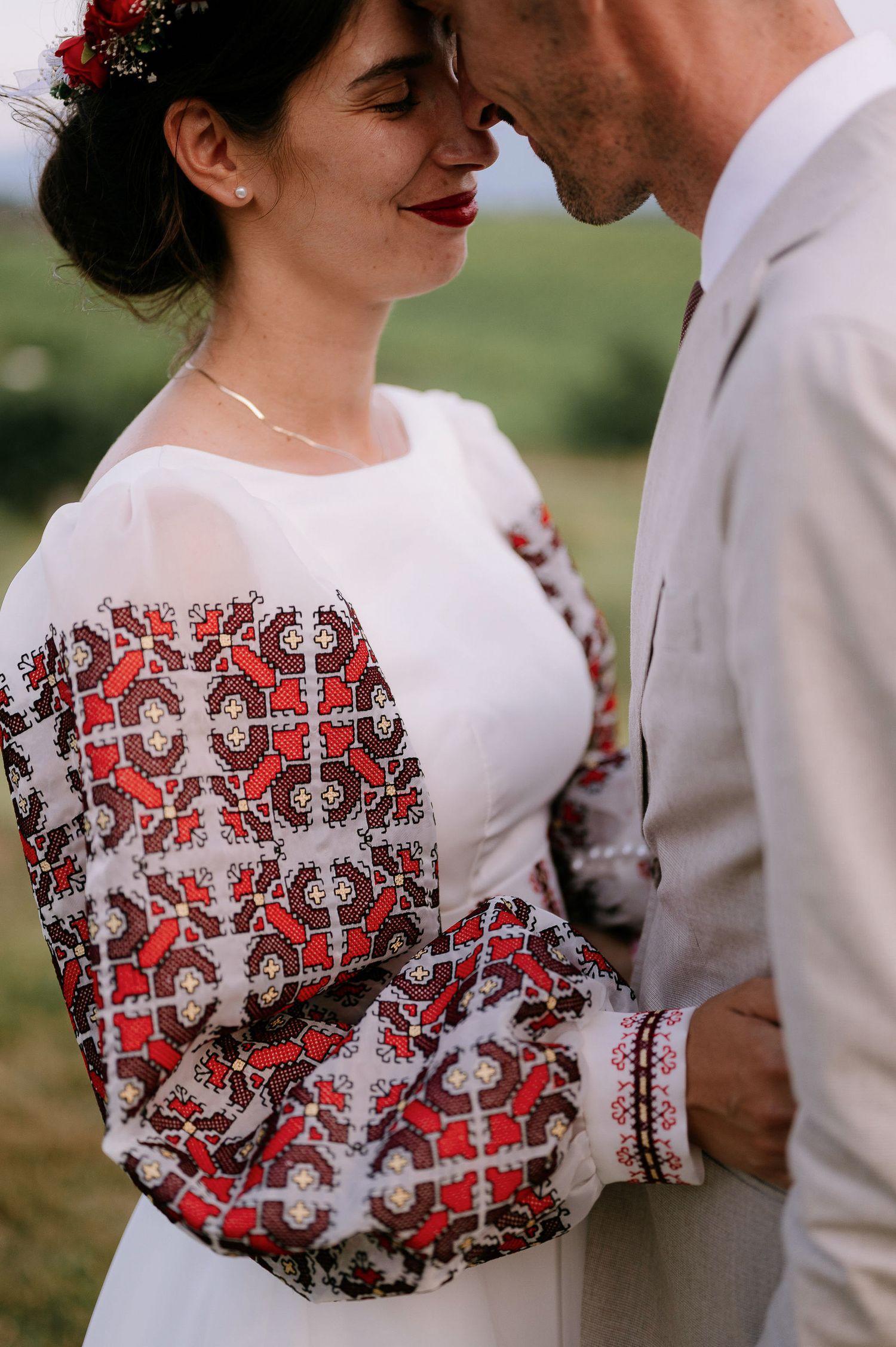Close-up detail of white wedding dress with intricate red and black embroidered pattern on sleeves.