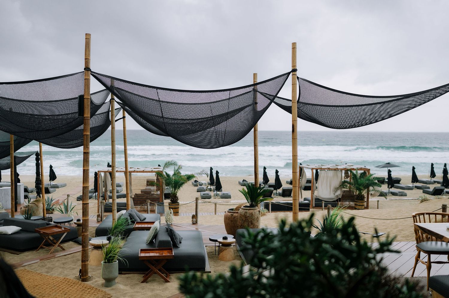 Beachside event setup with wooden poles and black mesh canopies overlooking the ocean.