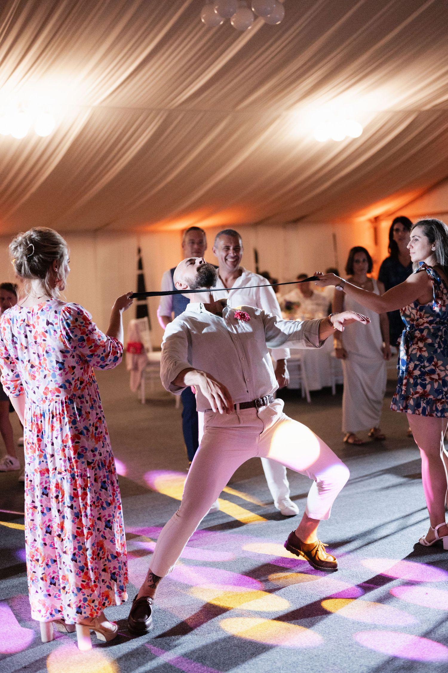 People dance in a row on a colorful illuminated dance floor under a white tent during a celebration event.