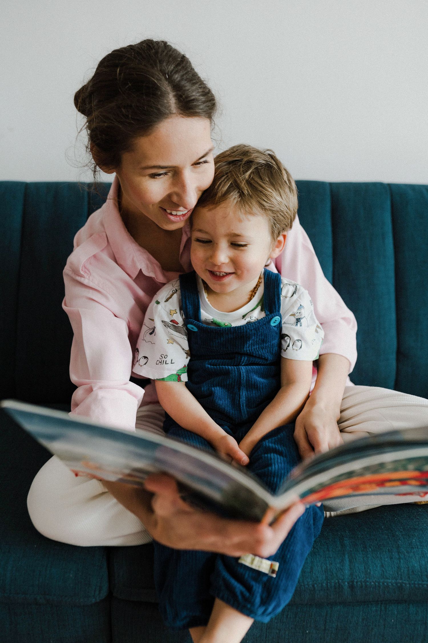 A parent and child share a tender moment reading a book together on a blue couch.