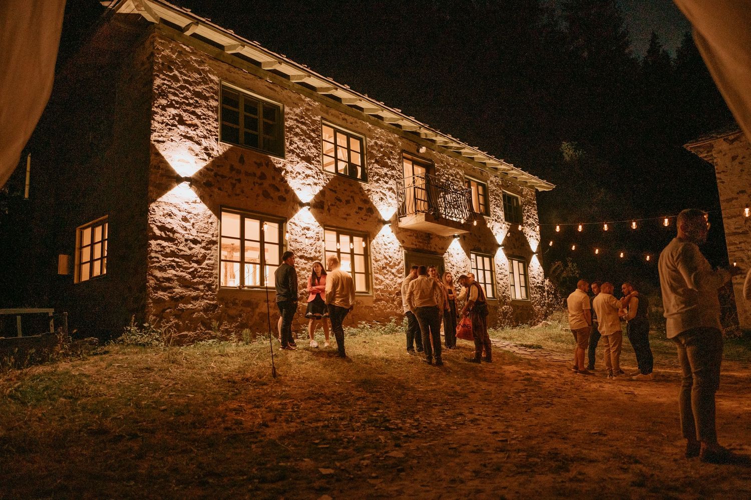 Stone building exterior lit by string lights creating a romantic nighttime atmosphere.
