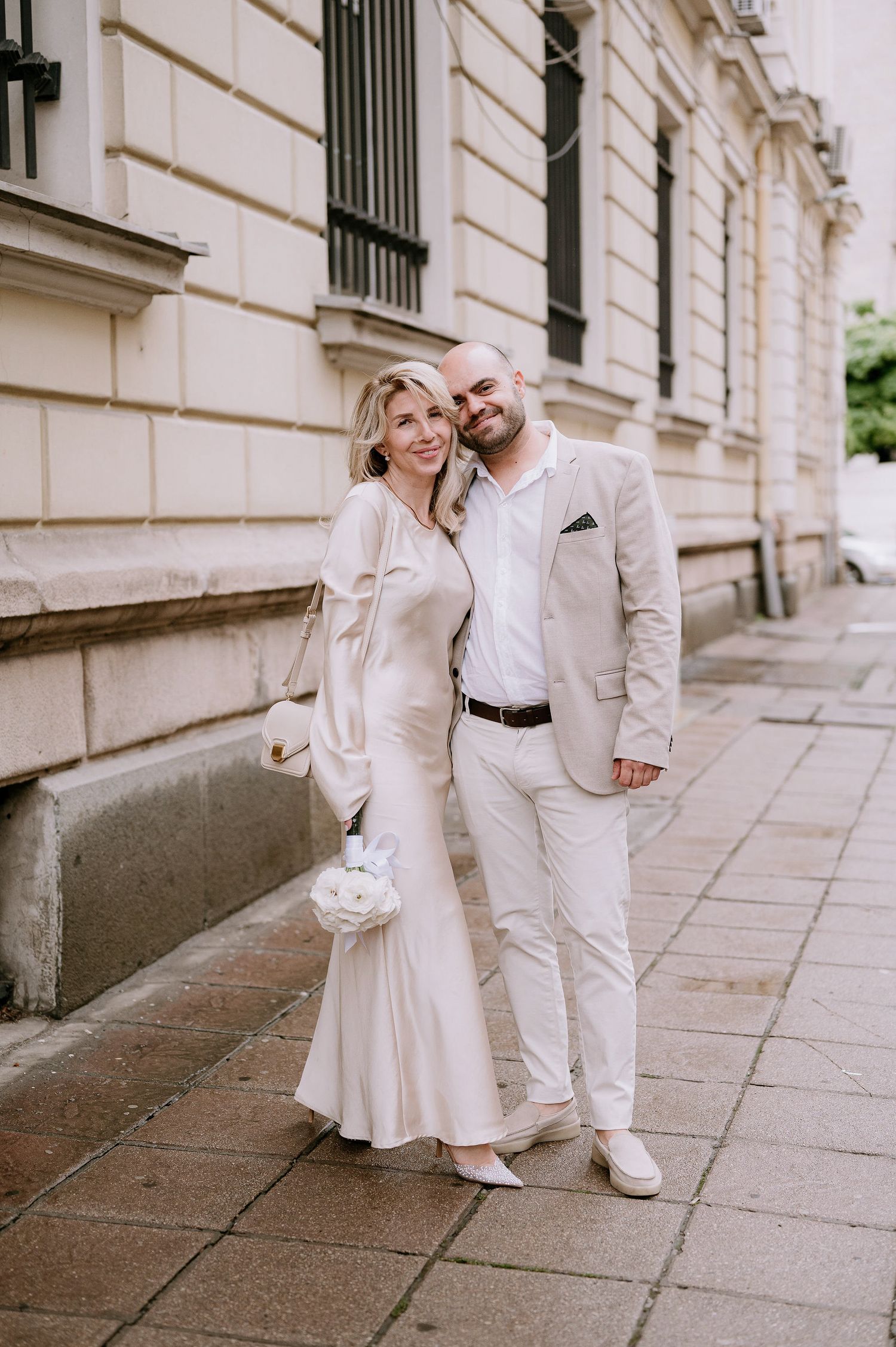 A romantic wedding couple shares a tender moment along a historic building walkway.
