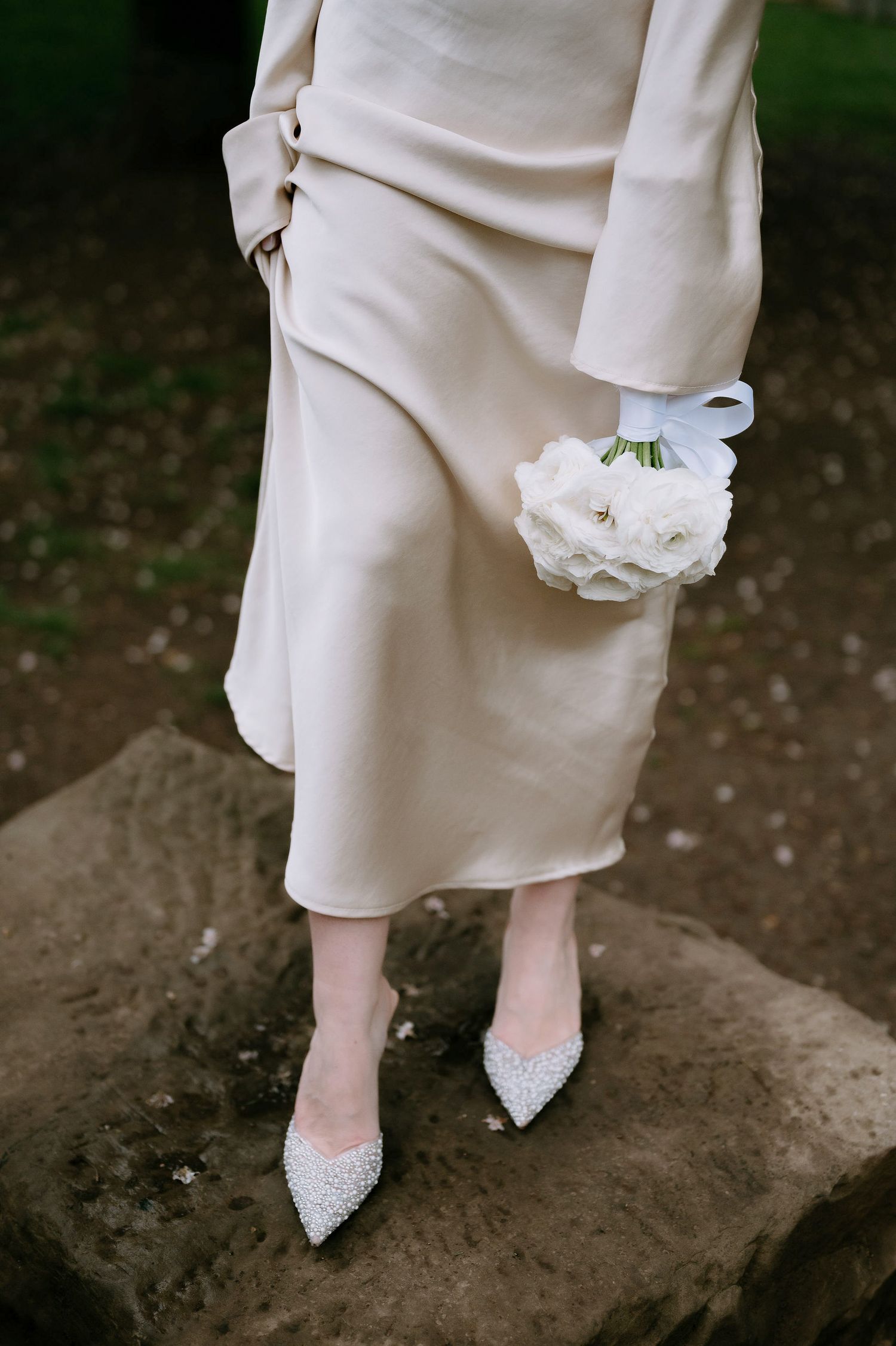 Sparkly bridal shoes and flowing white dress captured on rocky outdoor terrain.