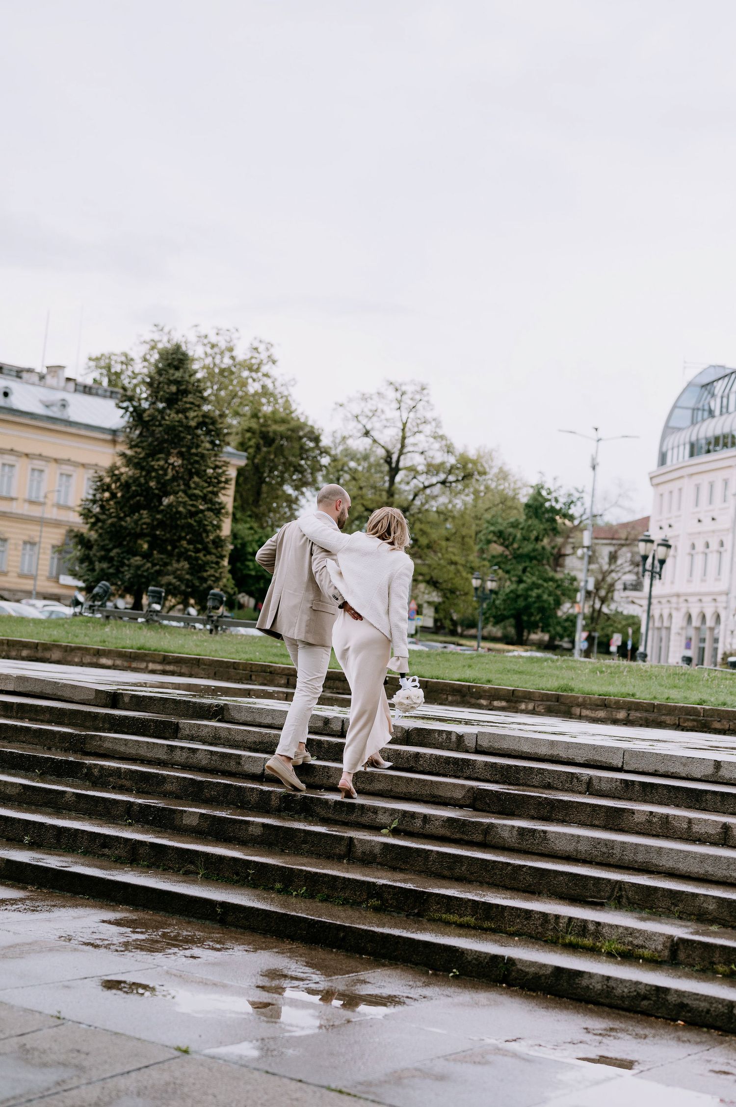 Two people in white clothing ascend wide stone steps in front of a classical architecture building.