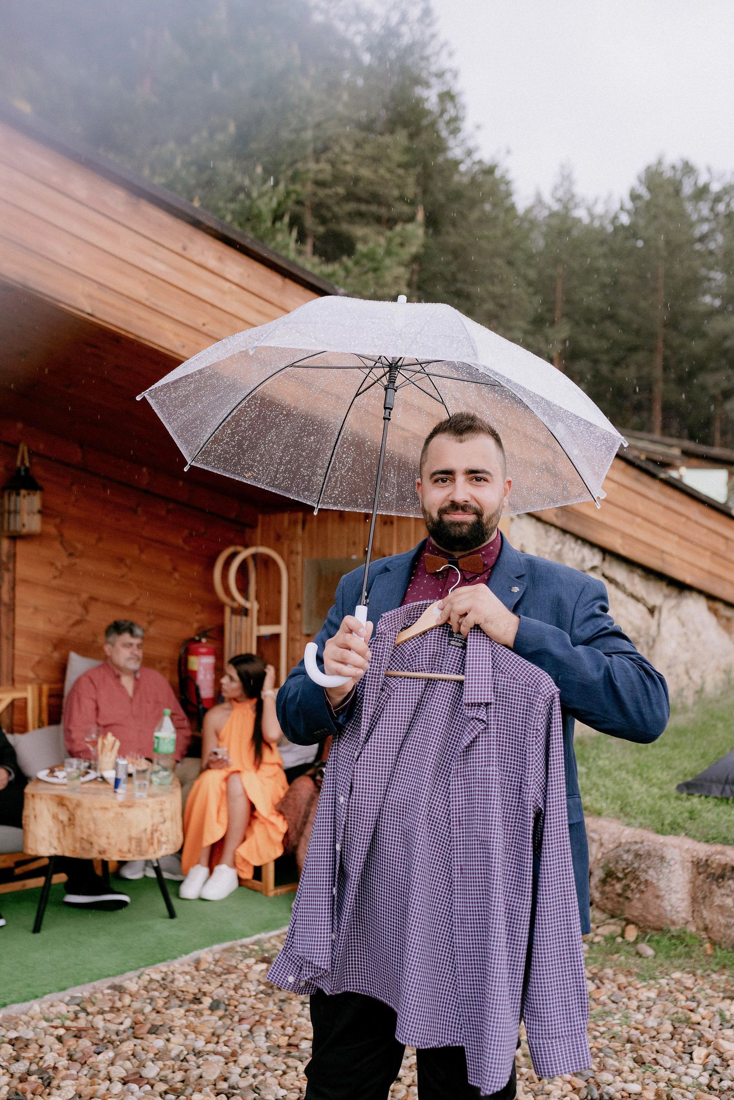 Someone holding a clear umbrella and purple garment outside a rustic wooden venue.