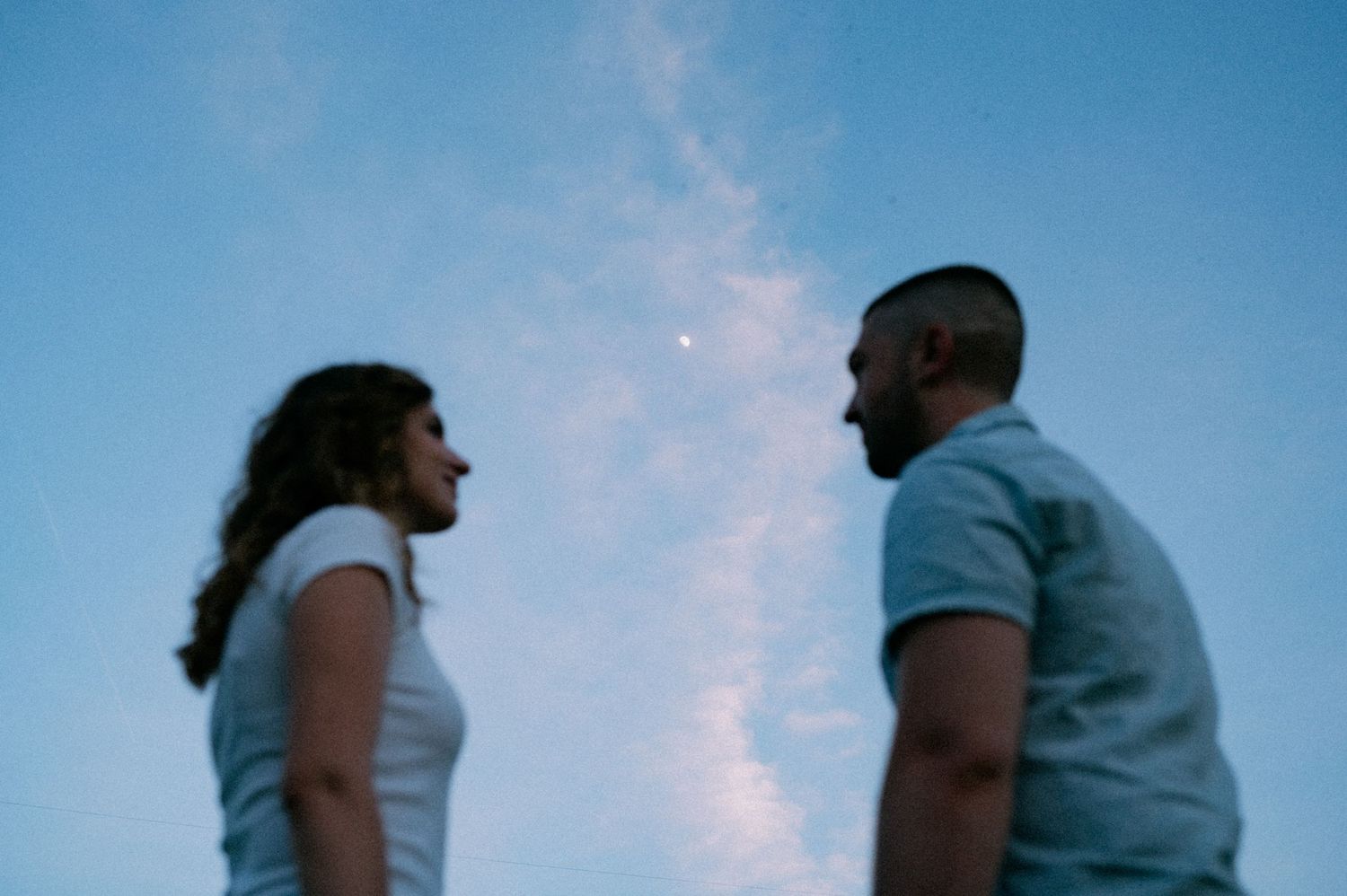 Two figures in profile gaze at each other against a twilight sky.