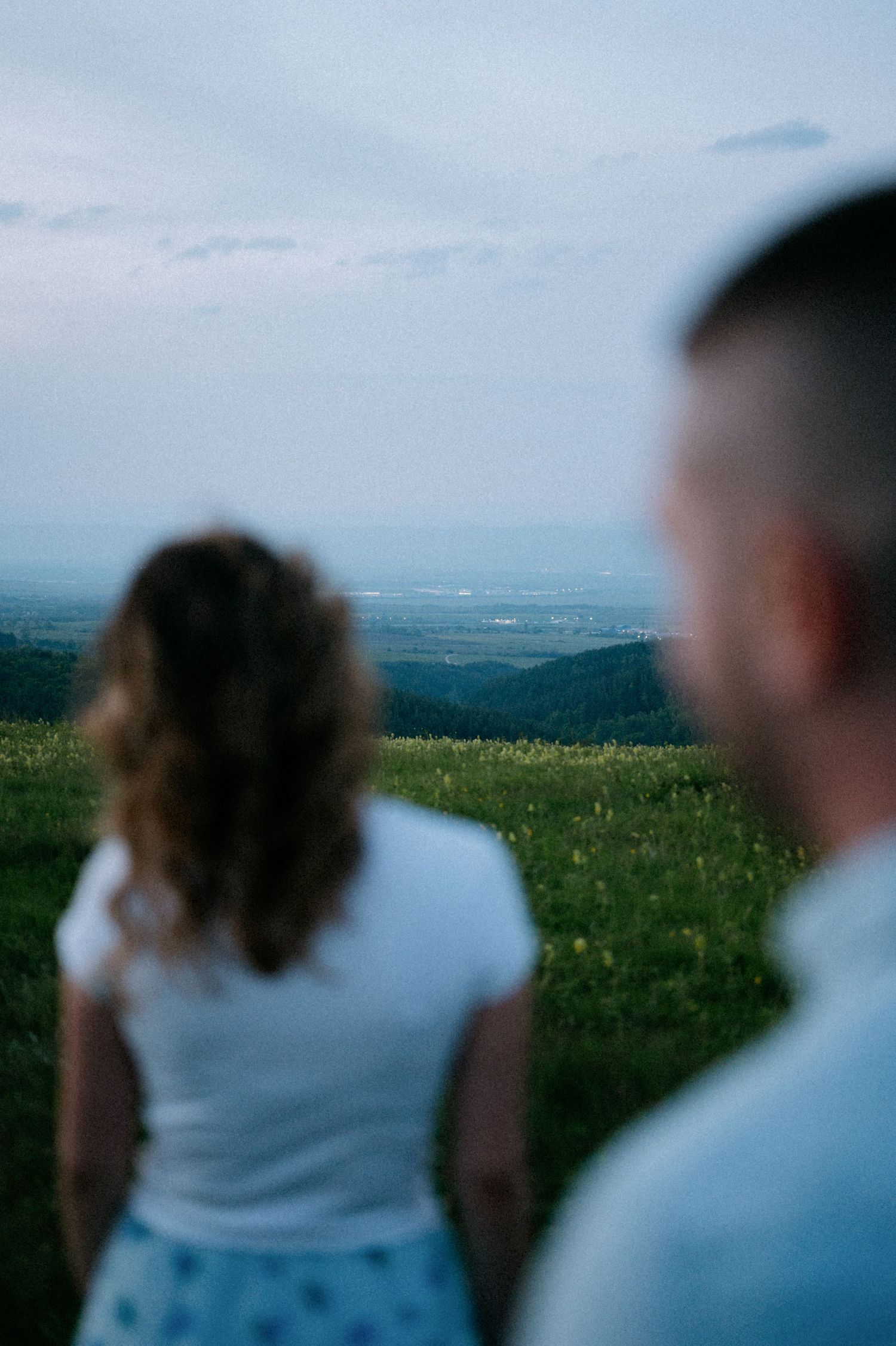 Blurred silhouettes of people standing on a grassy hilltop against a blue sky.