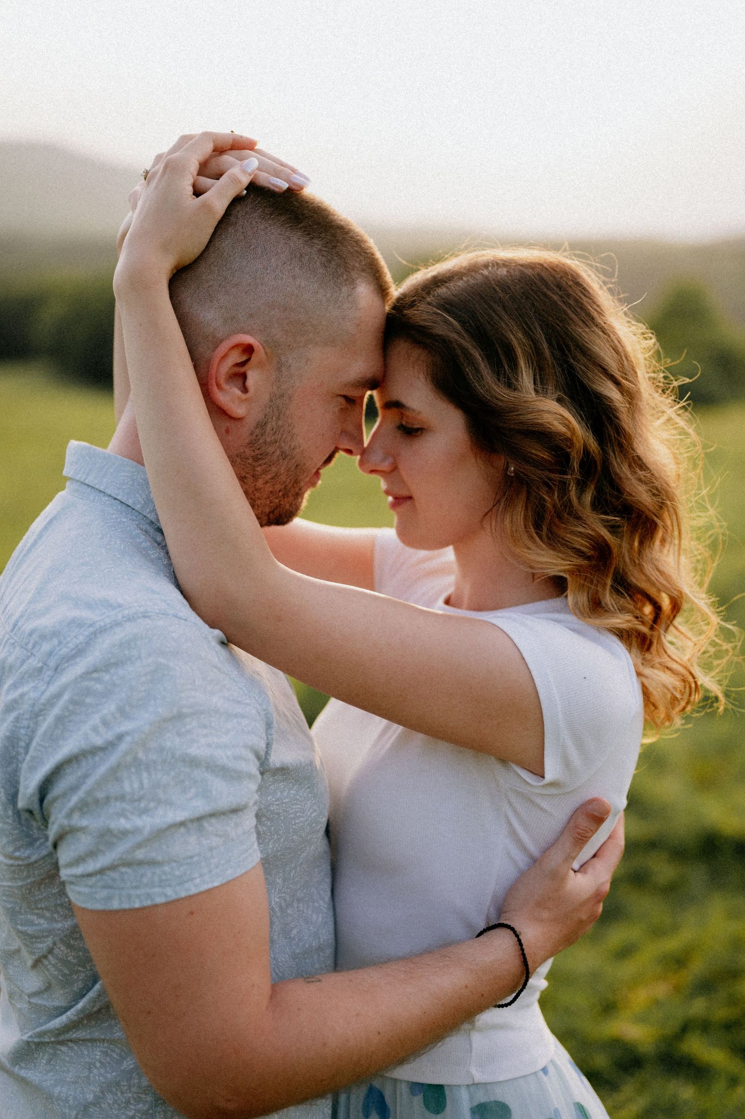 Close-up of couple dancing together in casual attire against natural landscape.