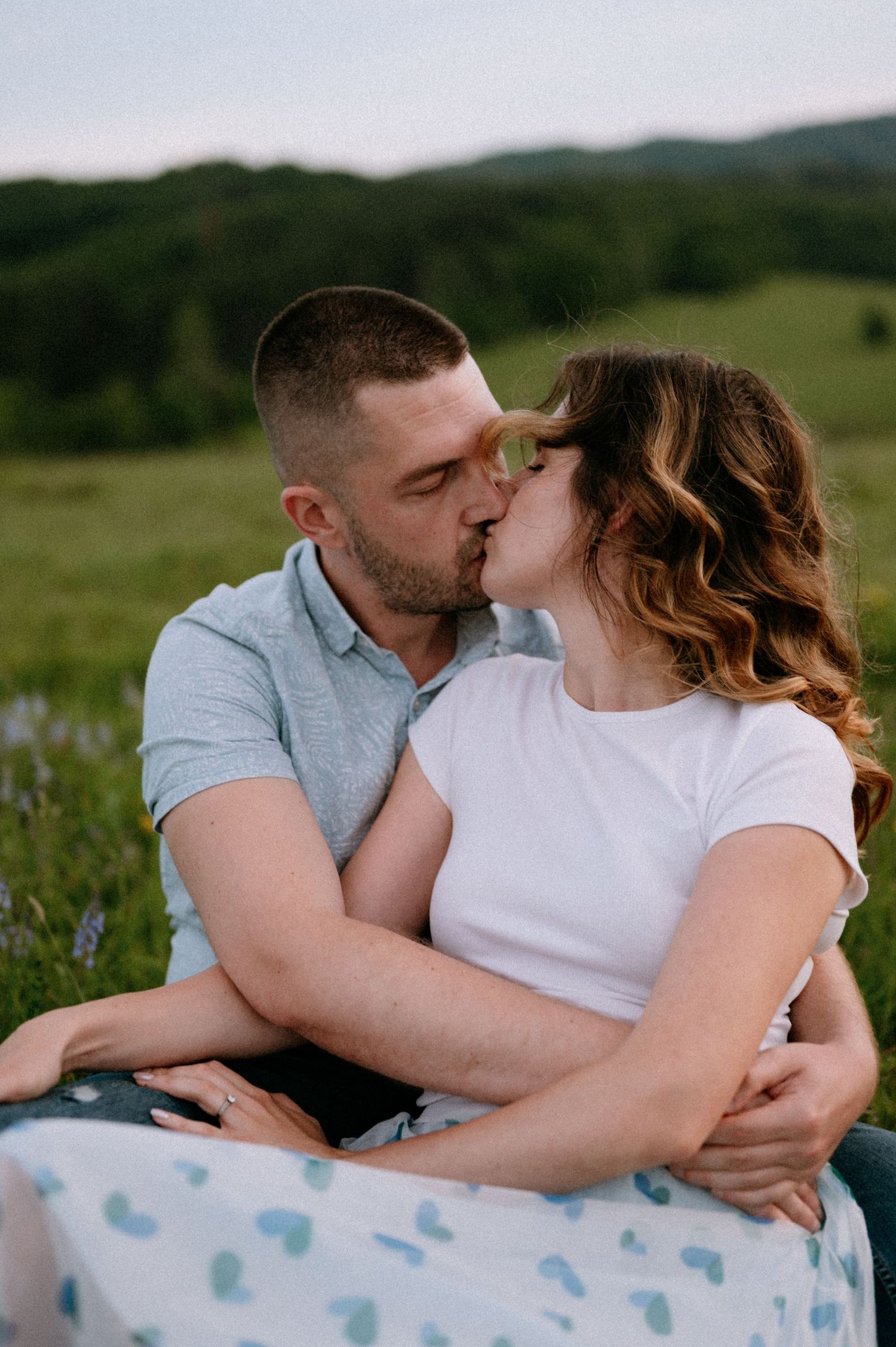 Intimate moment between couple on blanket with mountains and wildflowers in background.
