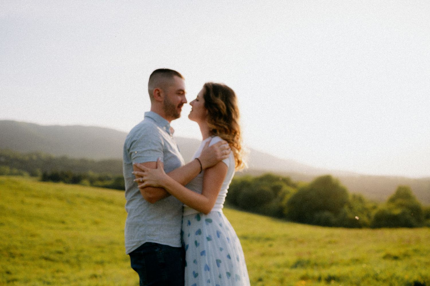 A romantic couple embraces in a golden meadow during sunset.