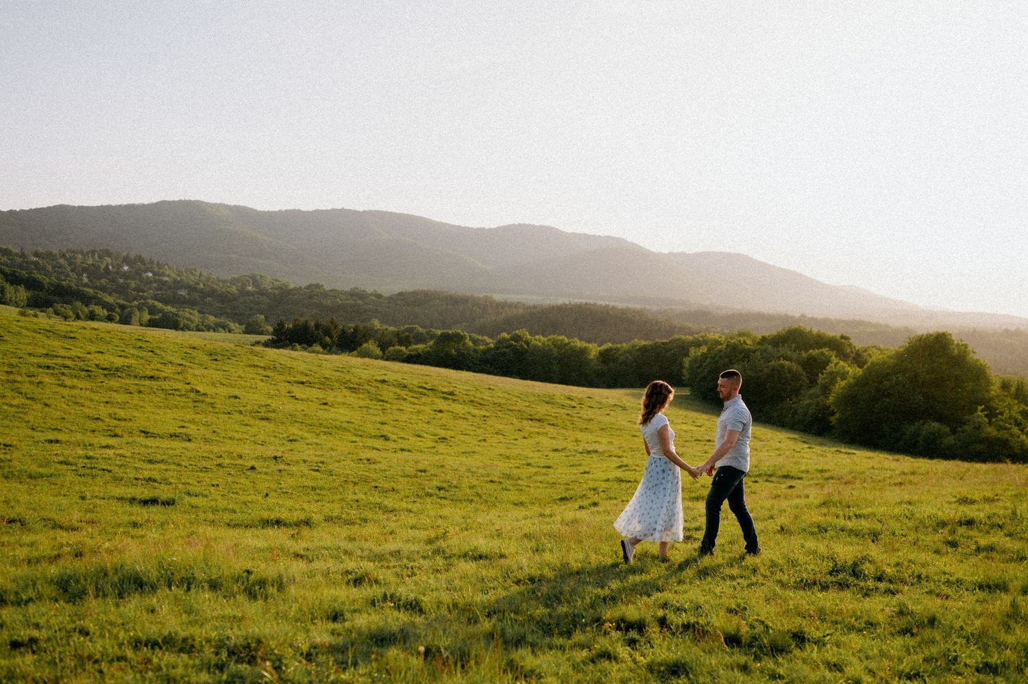 A couple strolls together across a scenic hilltop during golden hour.
