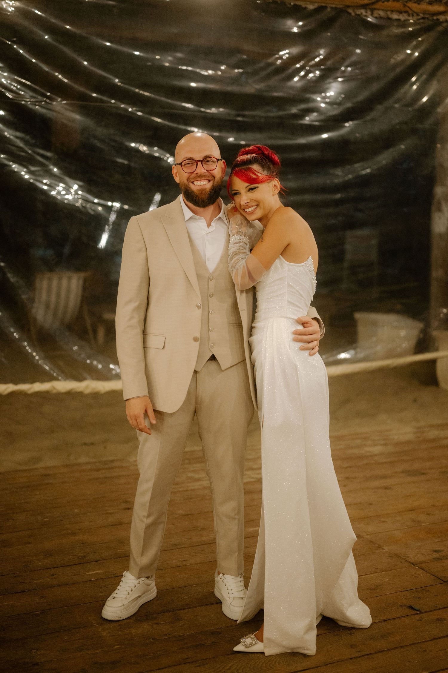 A couple in matching white sneakers dance together under a dark draped ceiling at an indoor celebration.