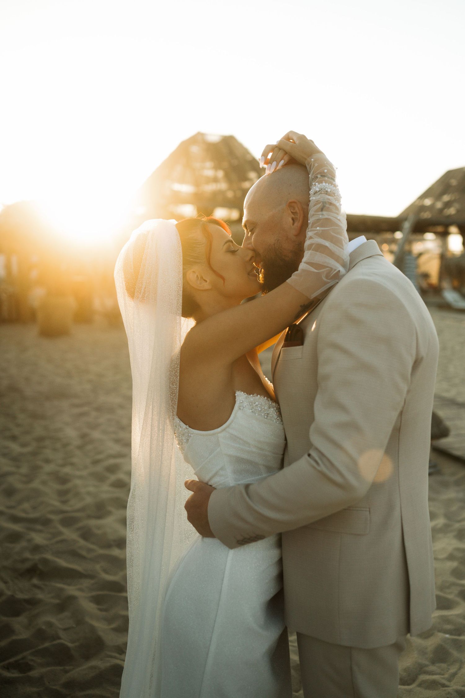 Romantic couple embraces on sandy beach at golden sunset during their wedding photoshoot.