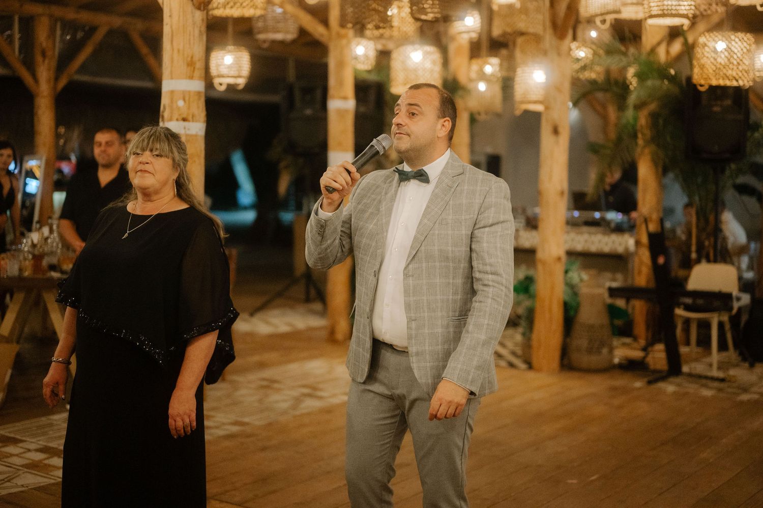 People dancing and celebrating at an outdoor evening wedding reception under wooden beams and string lights.