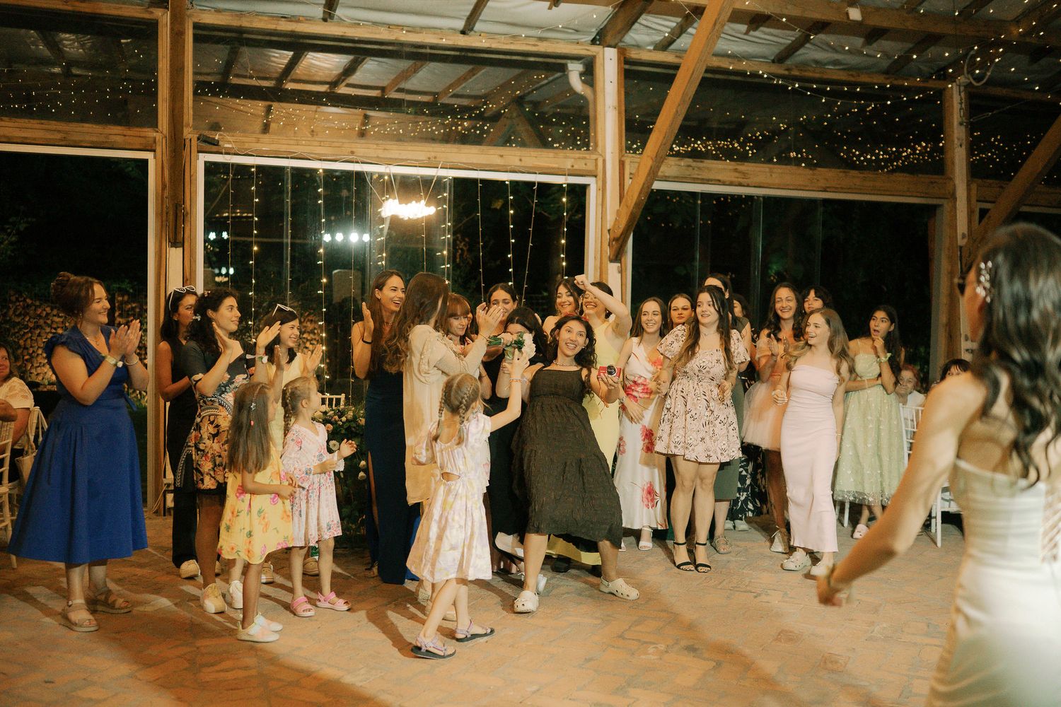 Wedding guests dance together on a wooden dance floor during an evening reception celebration.