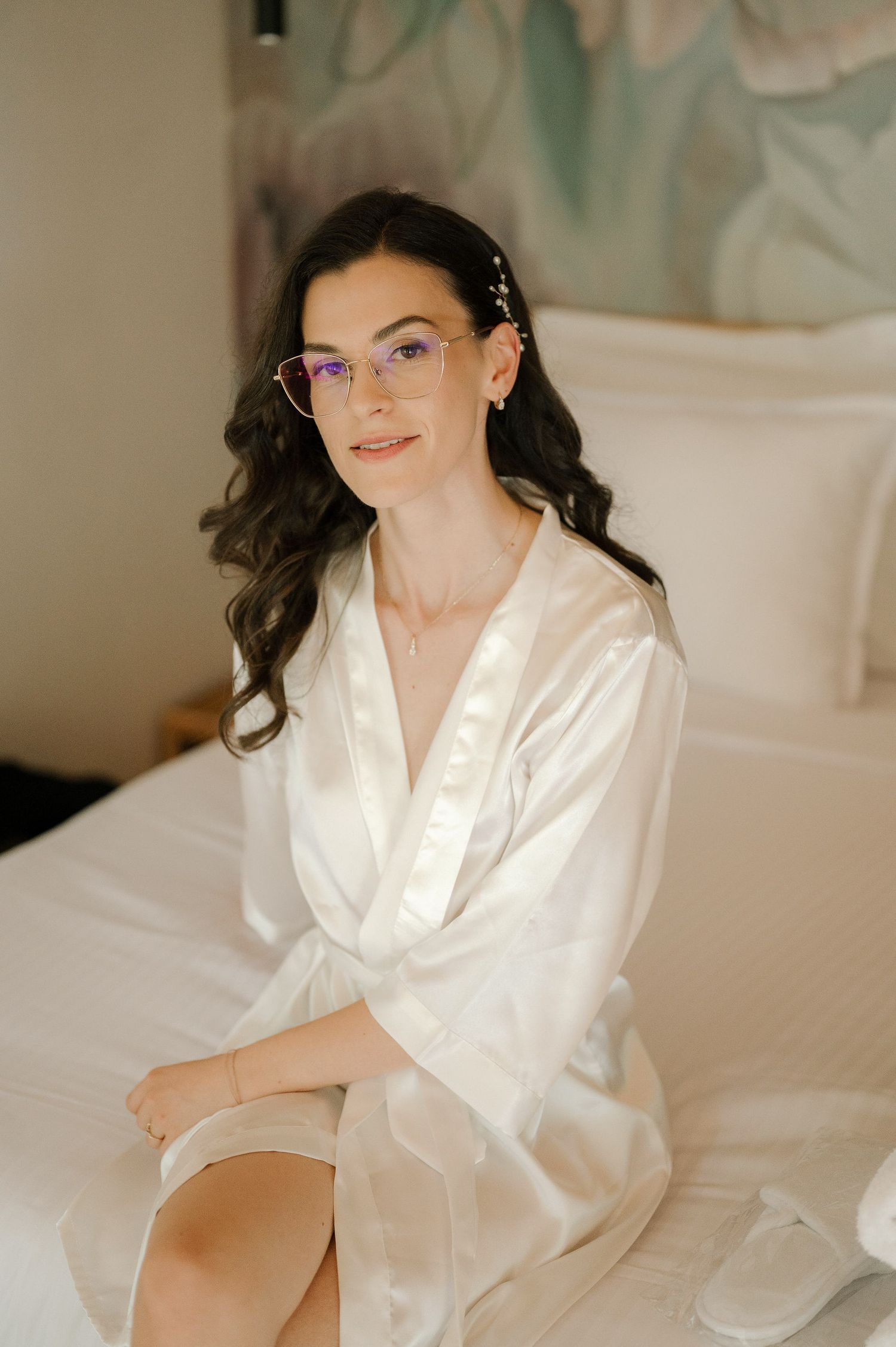 Person in white silk robe relaxing on white bedding in a bright bedroom setting.