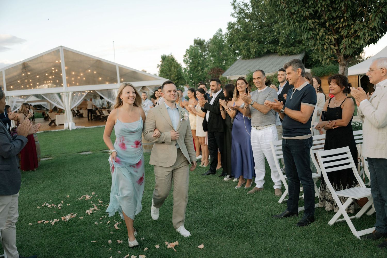 Wedding guests line up outdoors to watch a couple dancing at a garden reception celebration.