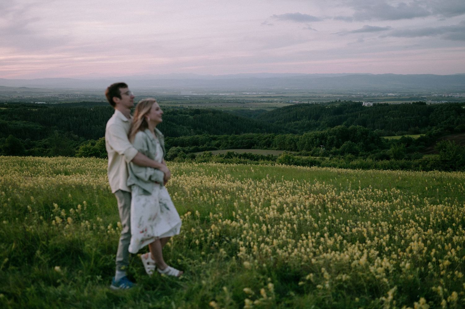 A romantic moment captured in a hilltop meadow with mountains visible in the distance.