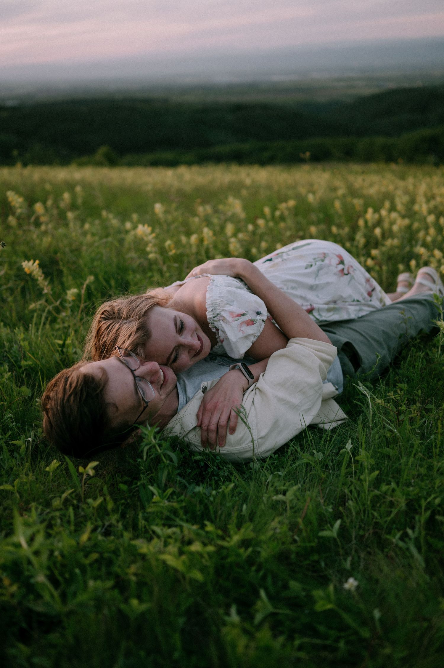 A romantic scene unfolds as two people rest in a flowering meadow at dusk.