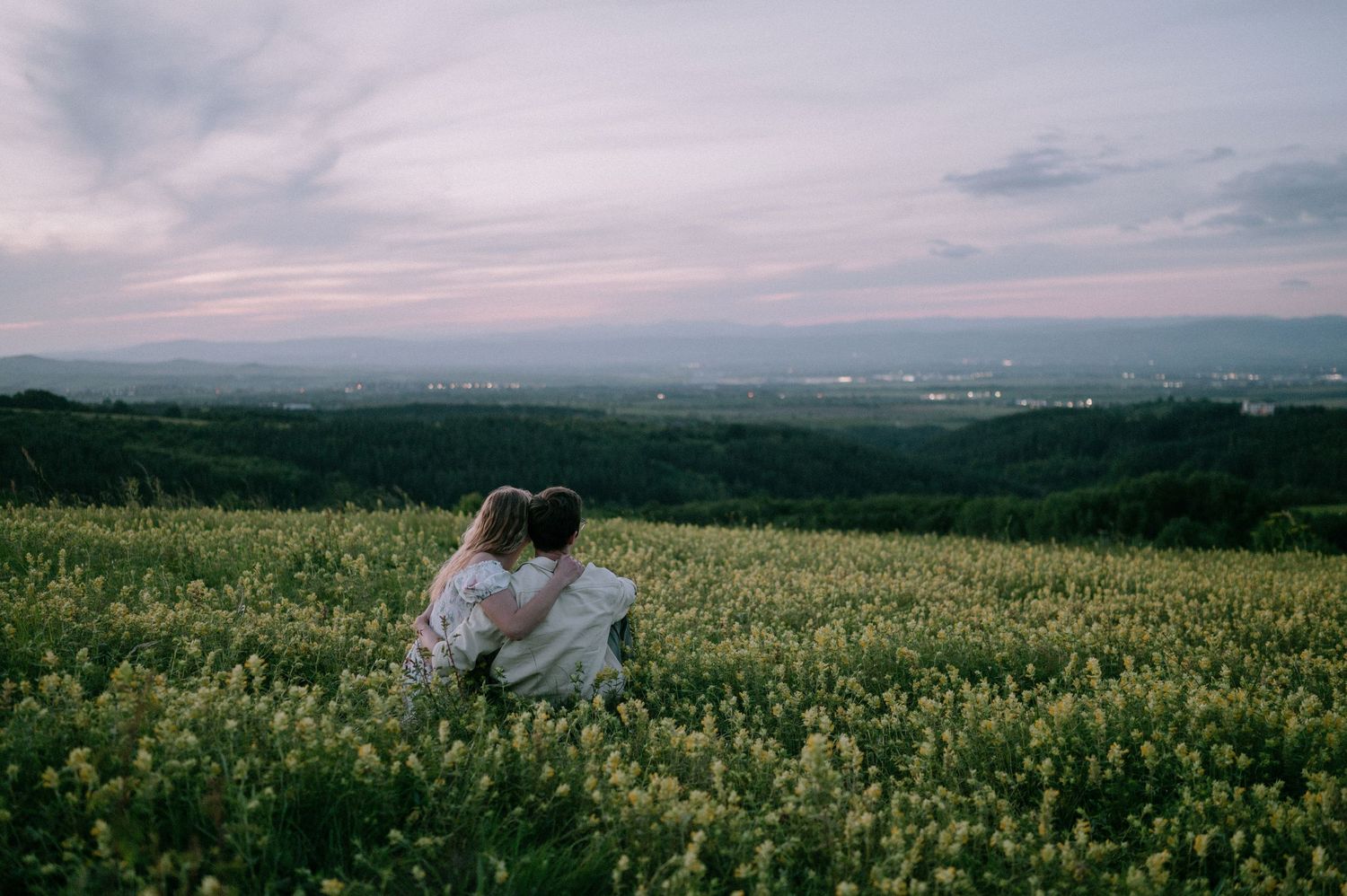 Wide landscape view of rolling hills covered in yellow flowers at dusk.