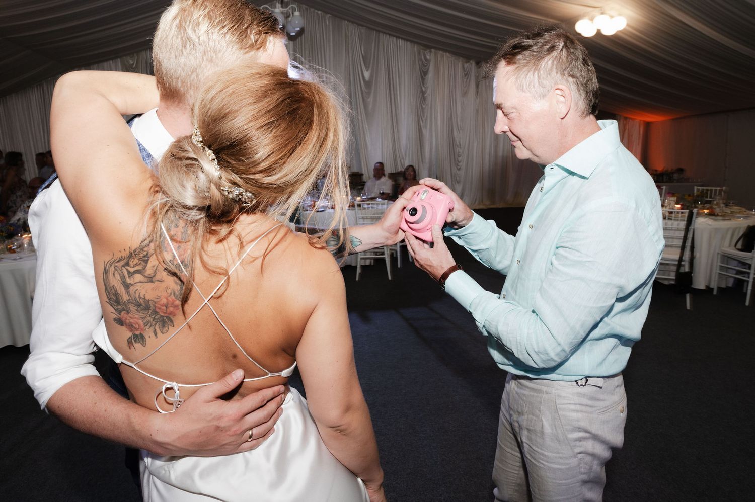 A couple shares a romantic dance together during what appears to be a wedding reception in a tent venue.